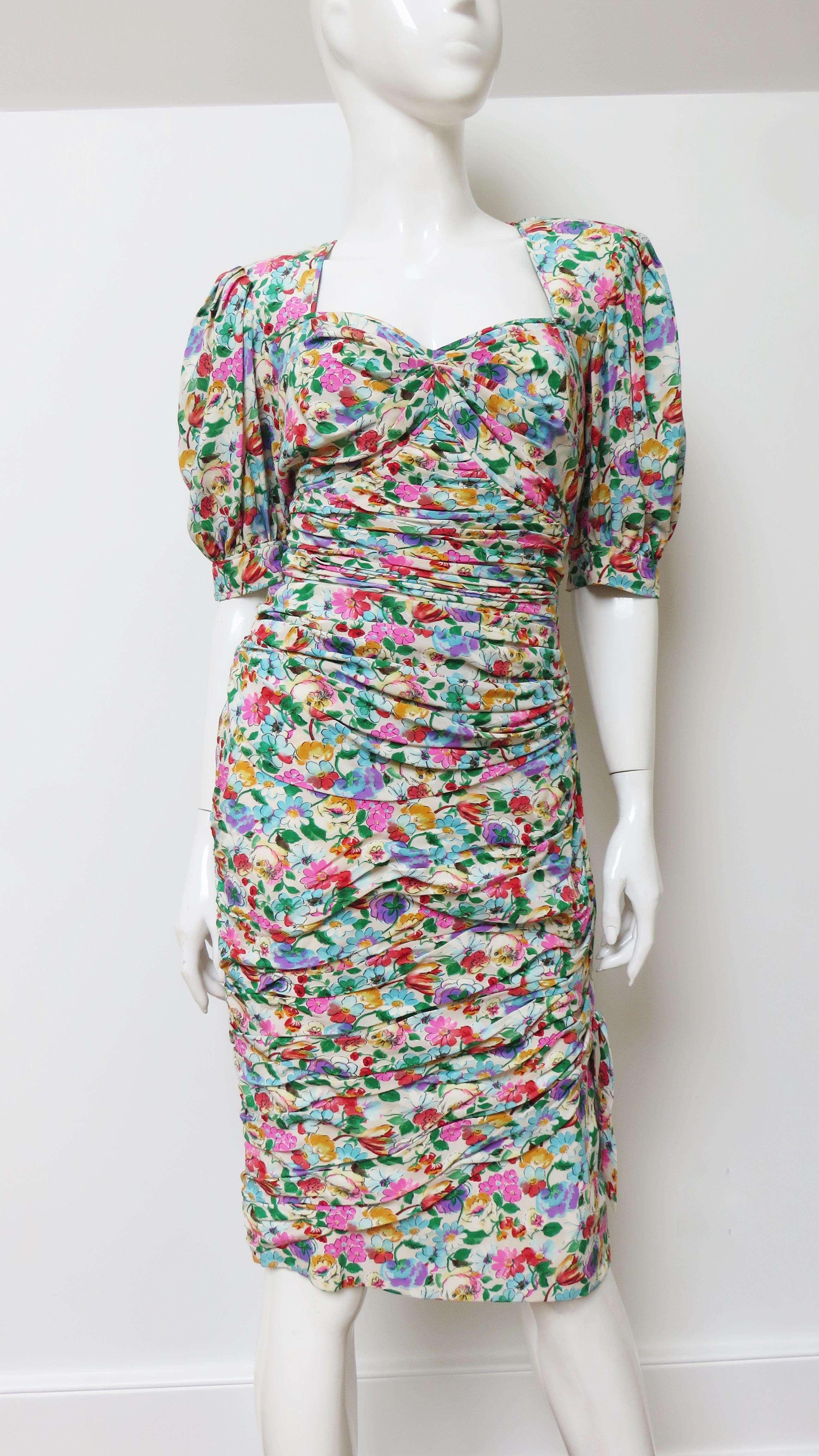 A very pretty flower pattern silk dress from Emanuel Ungaro in pinks, blues, greens and golds on an off white background. It has a sweetheart neckline, elbow length puffed sleeves with ties and is horizontally ruched front and back through to the