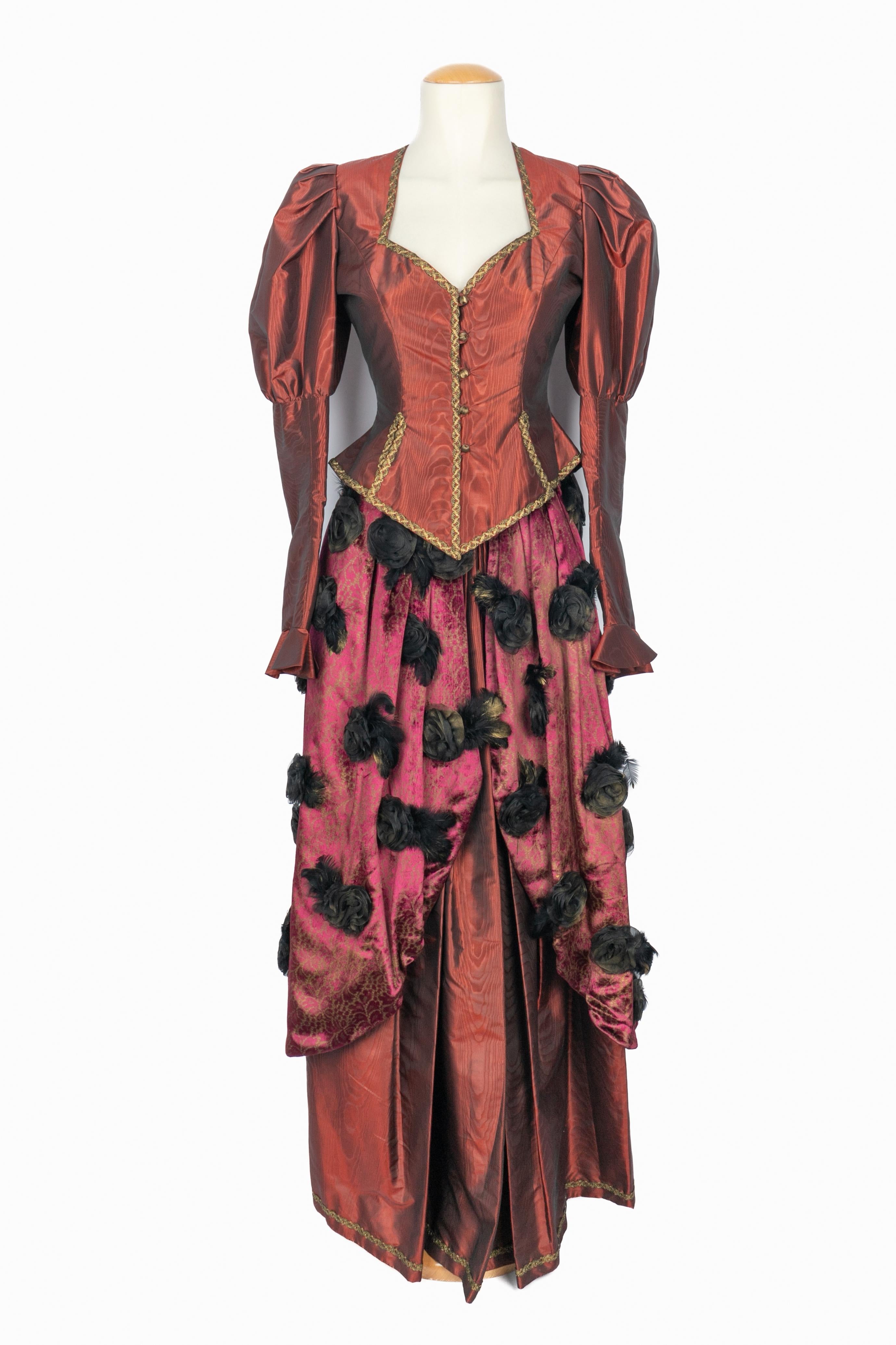 UNGARO - (Fabriqué en France) Robe de soirée en moire bourgogne. La jupe est recouverte d'une draperie de velours ornée de fleurs en relief en faille et en plumes. Veste cintrée aux manches bouffantes et bordée d'un galon vieil or. Étiquettes de