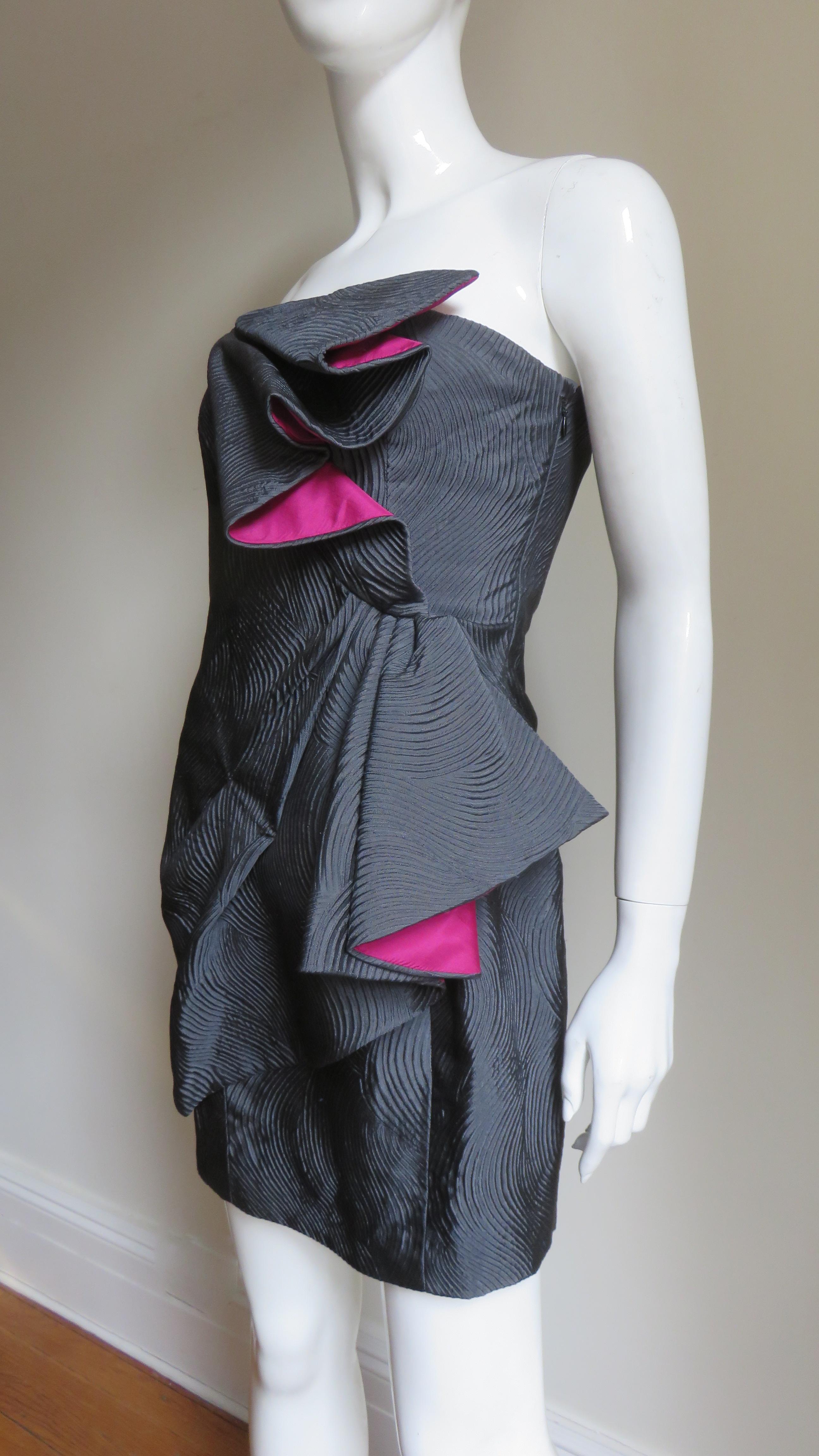 Un precioso vestido de seda gris marengo y rosa brillante de Emanuel Ungaro.  Es sin tirantes, con un panel frontal del corpiño doblado en diagonal con rosa brillante en el interior y otro en la cadera.  Tiene una cremallera lateral y está forrado