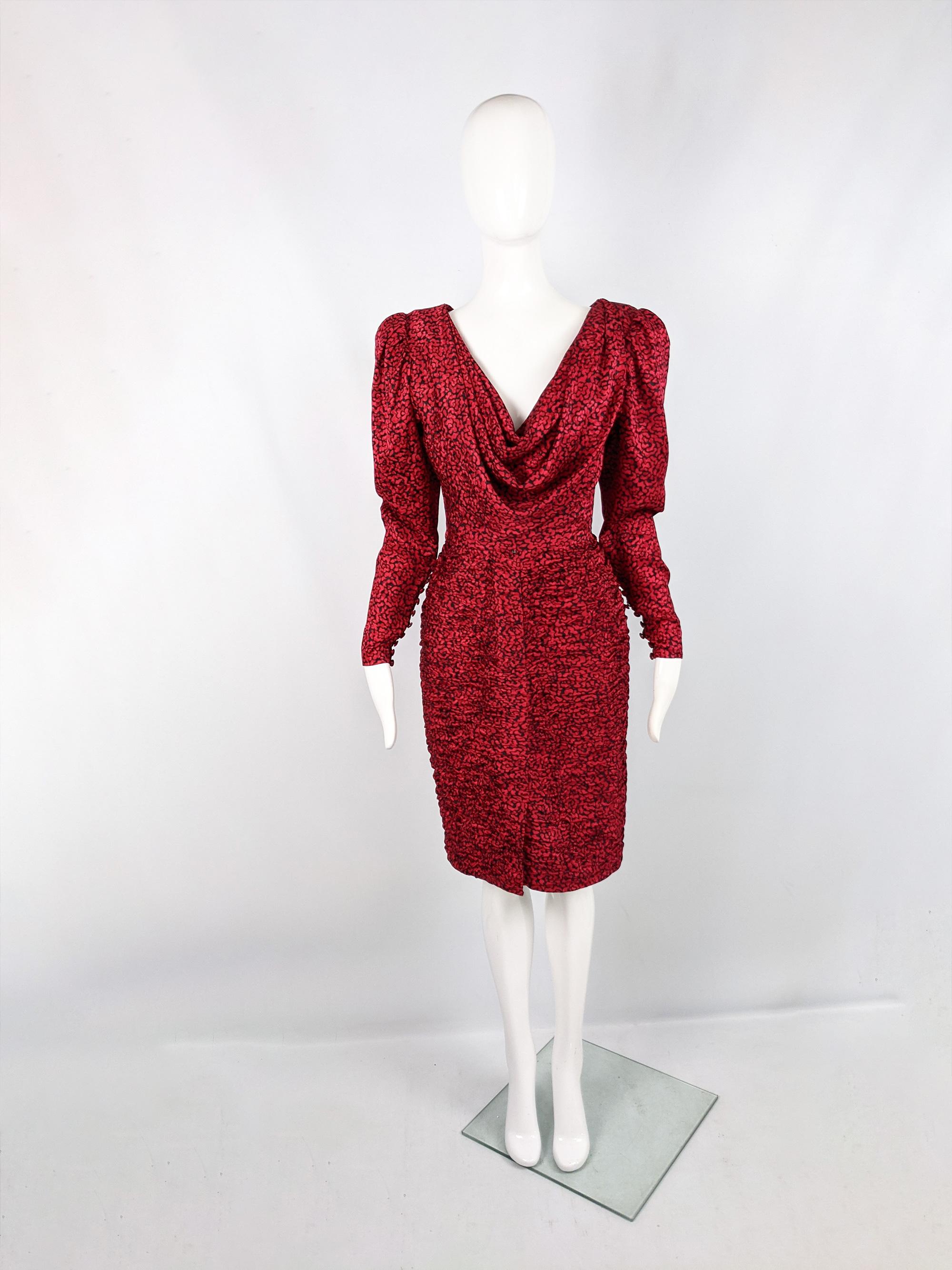 A stunning vintage womens party dress from the 80s by luxury French fashion designer, Emanuel Ungaro. In a red and black silk with a ruched skirt, deep, draped cowl neck and shoulder pads that puff out the sleeves to create a leg o mutton shape that