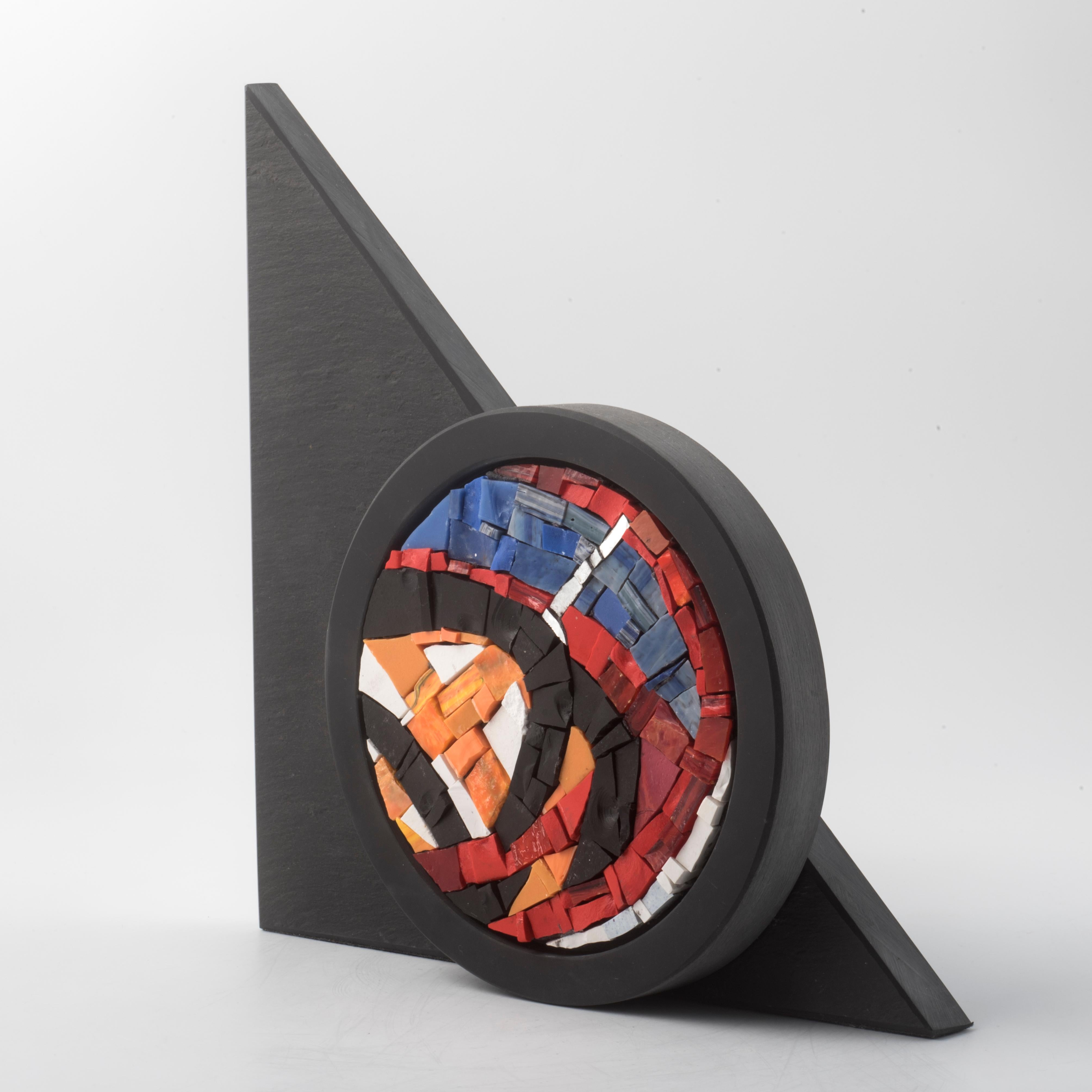 EMBLEME SOLAIRE  est une sculpture de table unique signée par l'artiste Nino Basso.
Composée de plaques d'ardoise naturelle et d'une mosaïque raffinée faite à la main en émail vénitien, l'œuvre allie minimalisme géométrique et expressivité