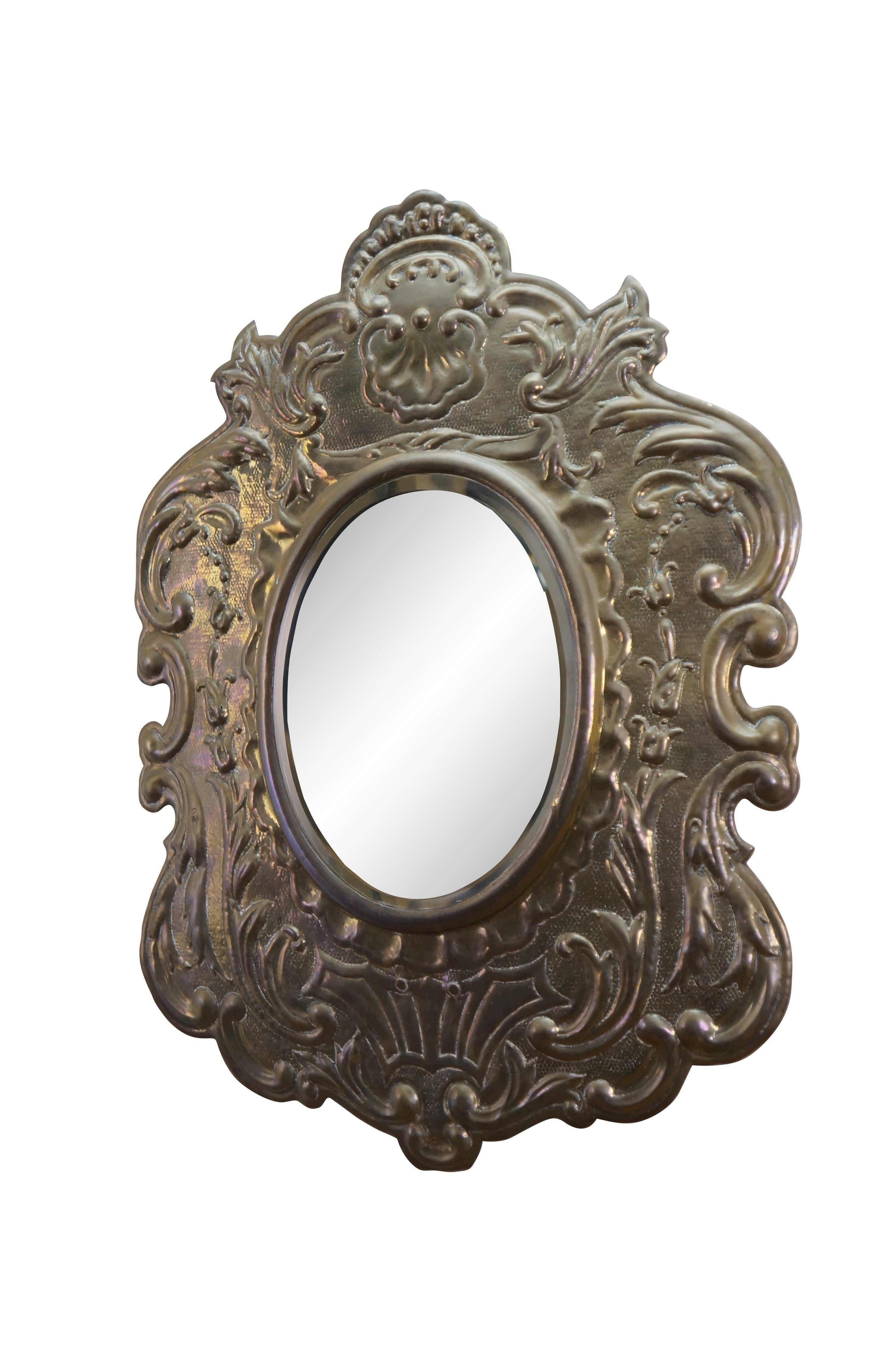 Vintage Repousse Baroque oval wall mirror with bevel edge, in a broad frame of ornately embossed brass, featuring foliate, scalloped, floral rose, and sea scroll designs.

Dimensions:
21.5