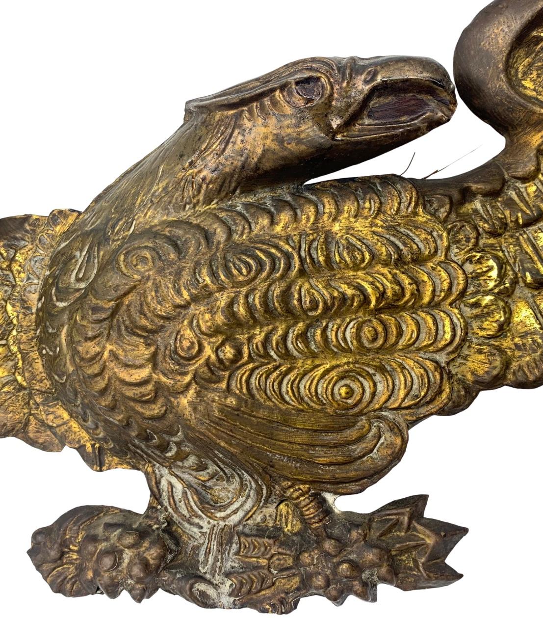 This is a vintage embossed brass American eagle, dating to the early 1900s. This is a striking eagle, with its wings fully outstretched. The eagle clutches an olive branch in its right talon and a bundle of arrows in the left. Traditionally, the