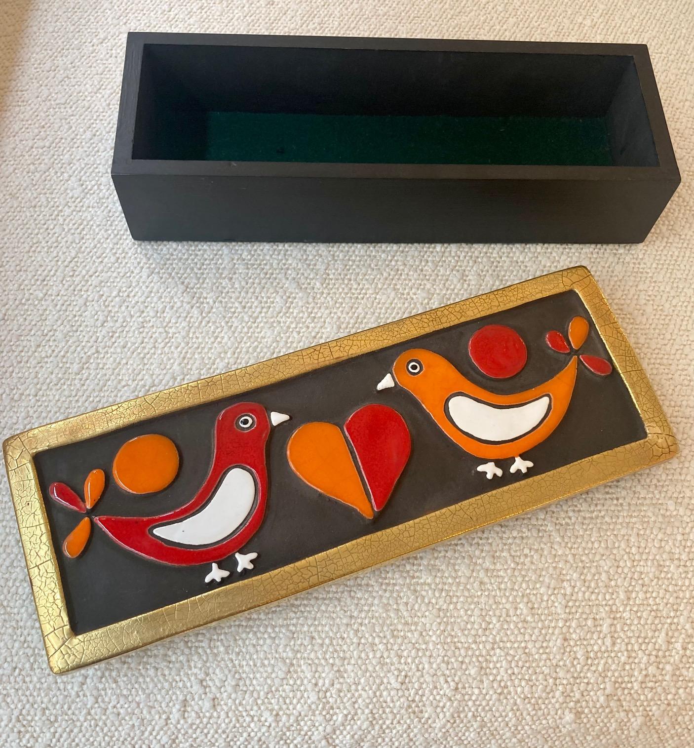 An enameled ceramic box sporting 2 doves facing each other and a heart in the middle.
Embossed earthenware enameled in red, orange and white on a black background. 
Crackled gold edges. 
the base of the box is in wood
Model 