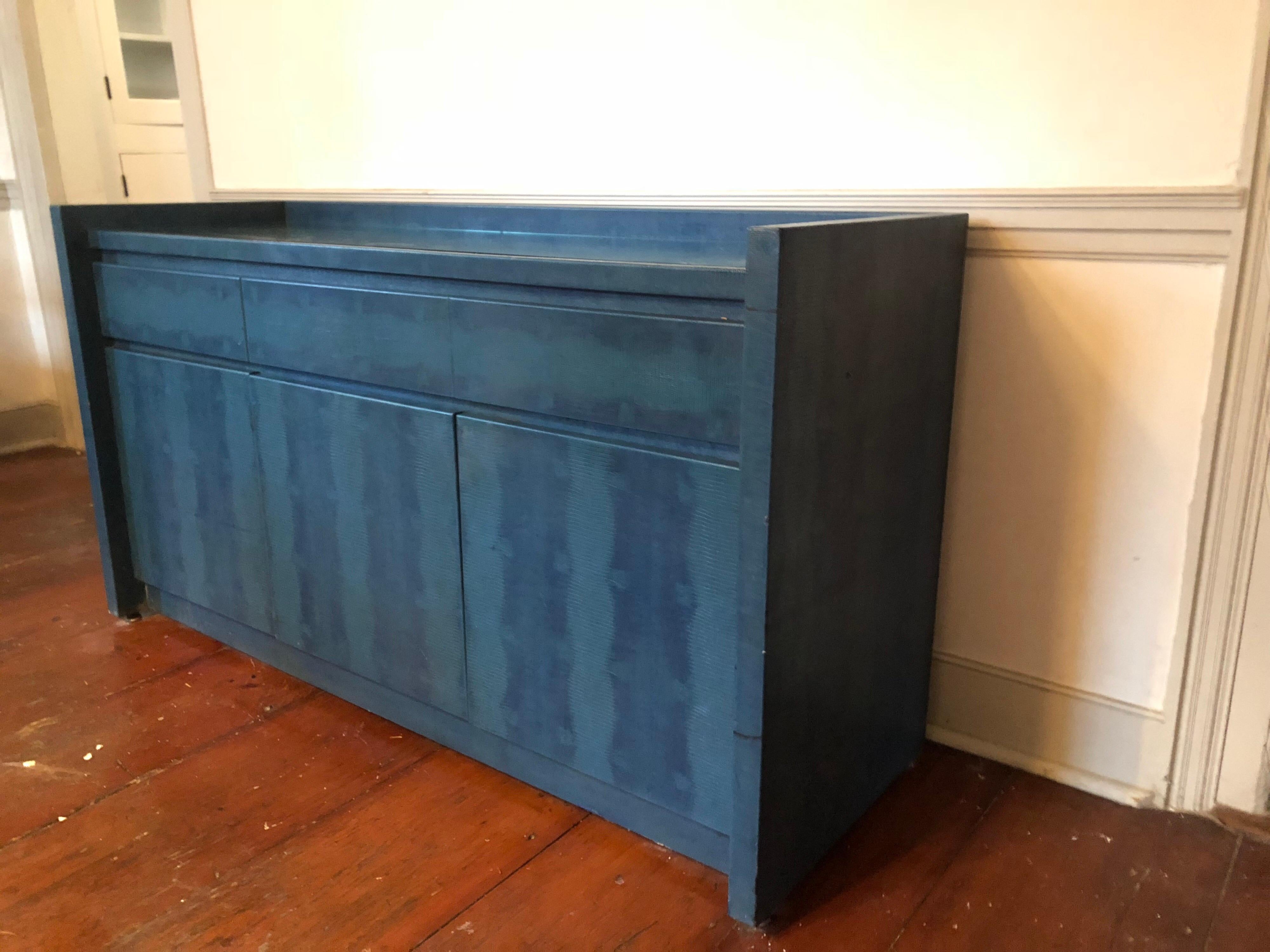 A embossed leather sideboard in a deep teal blue. Wonderful Parsons style with structured lines. Complete with fitted glass top. Three upper felt lined drawers and lower drawers with shelves.