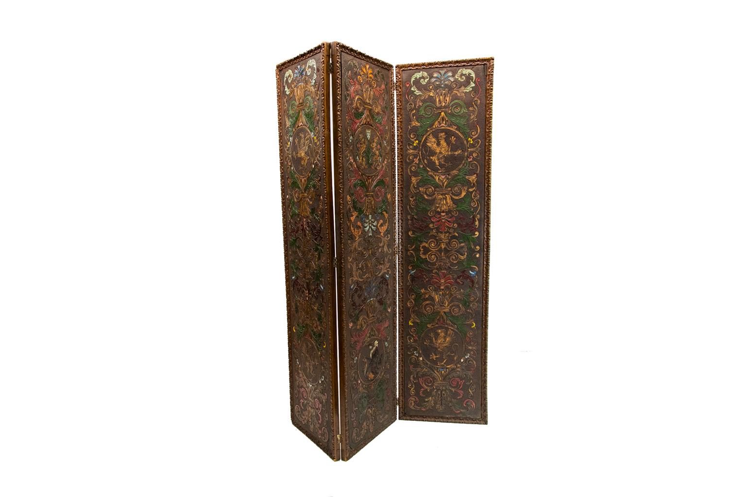 Embossed leather three-panel screen, hand painted with a lion crest and floral arabesques, it has a stipled background with beautifully carved wooden frames.
          