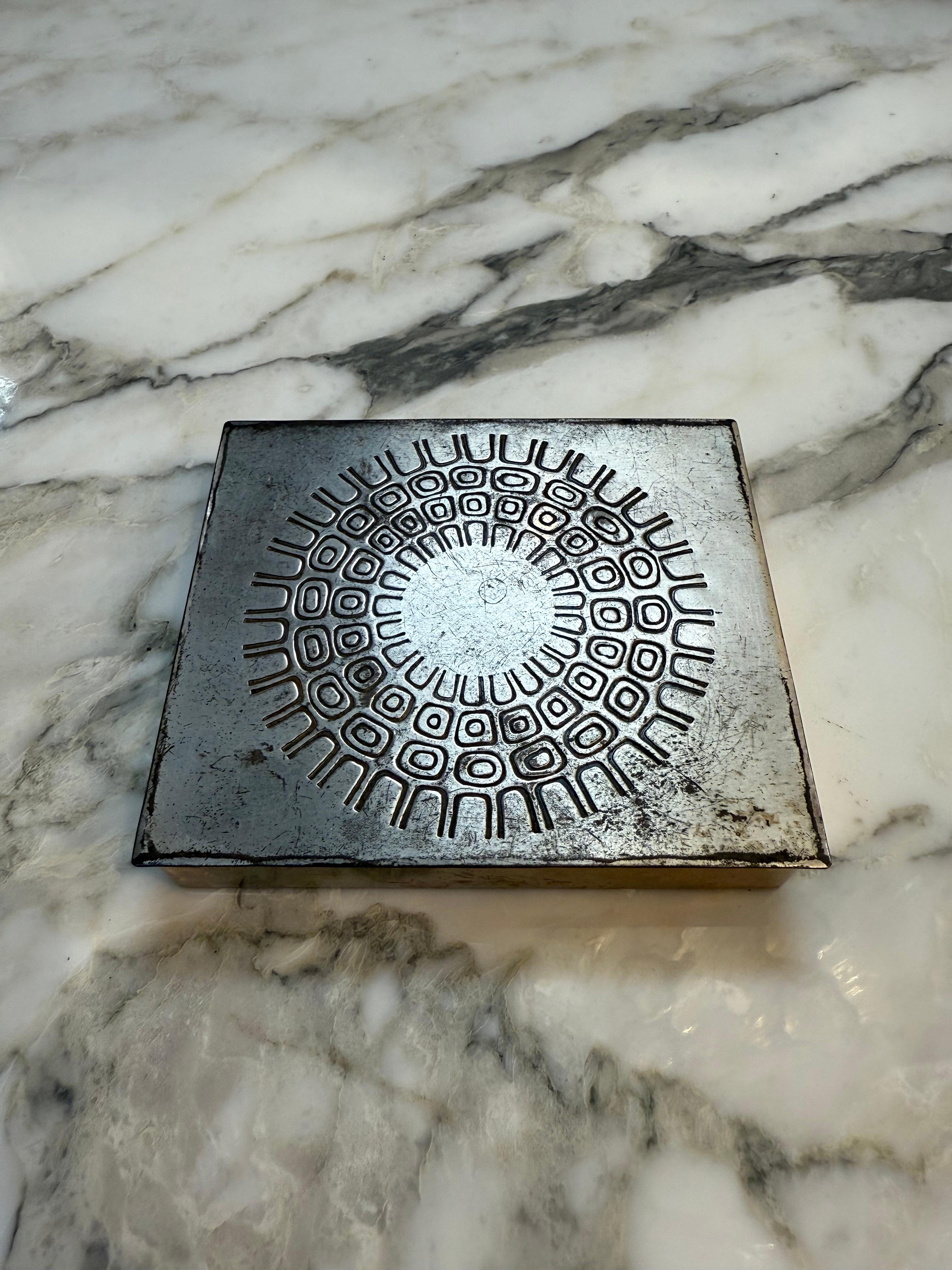 This striking mid-century modern box showcases a bold embossed geometric sunburst motif on its lid, radiating outward in concentric symmetry. The intricate pattern, inspired by abstract and atomic-age design, adds visual texture and depth while