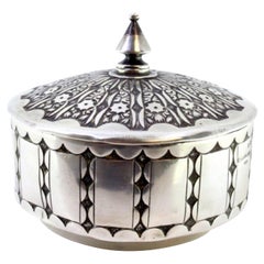 Embossed silver box with a circular shape and a knob on the removable lid