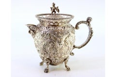 Embossed silver milk jug with female and elf faces, lion-handle lid, claw feet