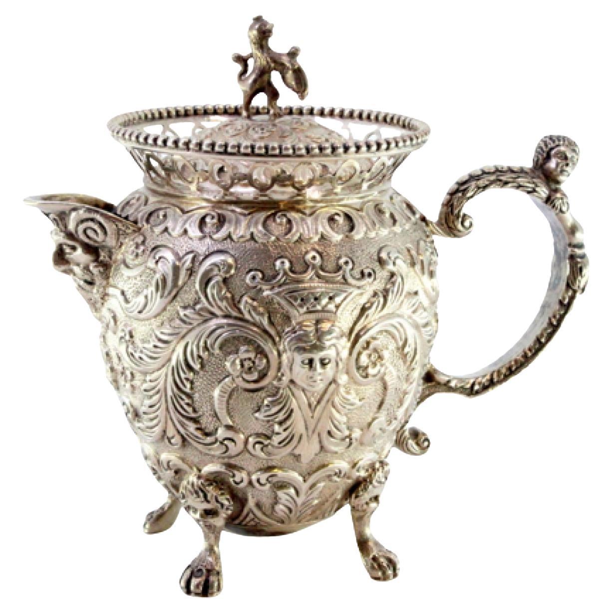 Embossed silver milk jug with female and elf faces, lion-handle lid, claw feet For Sale