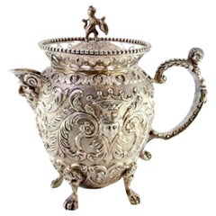 Embossed silver milk jug with female and elf faces, lion-handle lid, claw feet