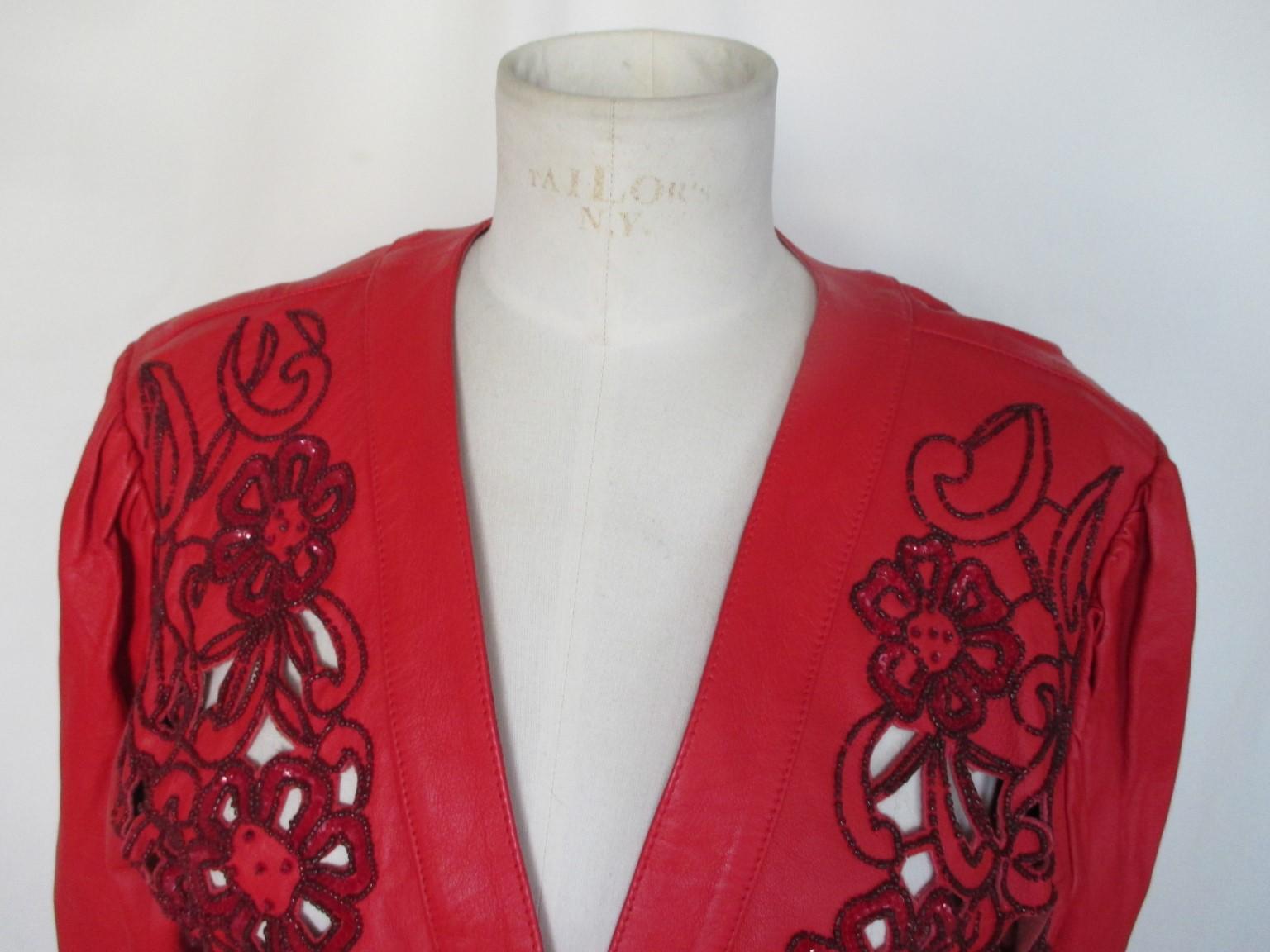 Il s'agit d'une veste boléro en cuir rouge vintage unique. 

Nous proposons d'autres articles exclusifs, consultez notre boutique en ligne.

Détails :
Broderie fleurie ouverte sur le devant en cuir avec perles, se porte comme un boléro.
Vers les