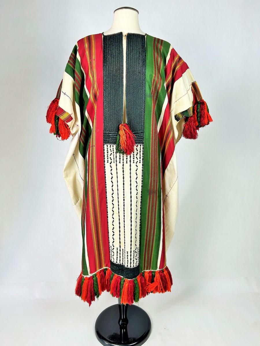 Circa 1950
Tunisia

Large festive or ceremonial blouse in white cotton applied with Tunis silk ribbons, a tradition since the 18th century. Tightly embroidered breastplate in black floche silk and silk tassels in the same colour adorn the shoulders