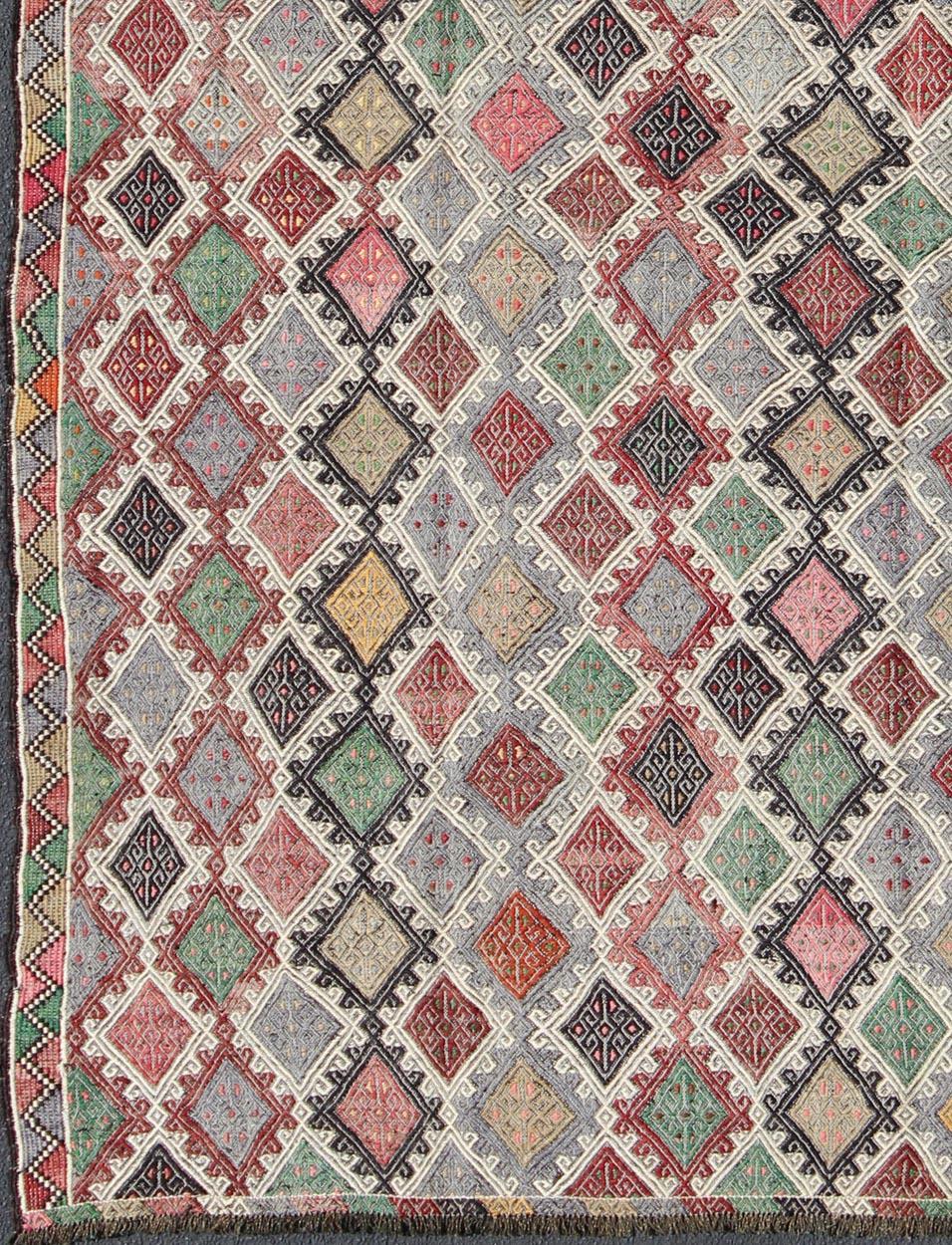 Questo meraviglioso tappeto Kilim ricamato geometricamente presenta un motivo a rombi sullo sfondo e un bordo sobrio, abbinato a una serie distinta di colori casuali come rosa, grigio, verde, blu, avorio, rosso, nero, crema e giallo. 

Misure: 6'8''