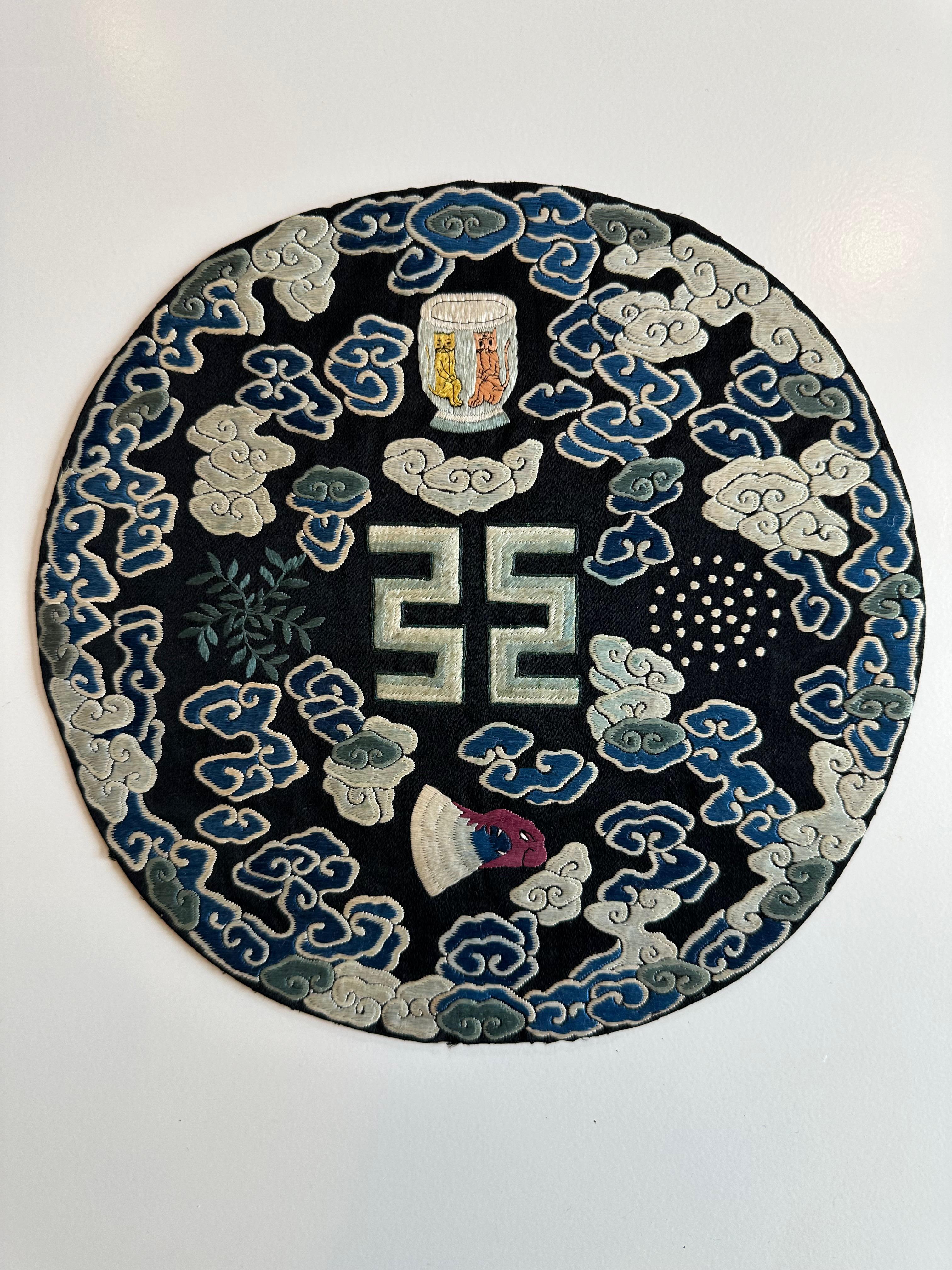 This medallion, which would have been sewn on a robe, depicts a number of symbols on a background of light and dark blue clouds. The central symbol is Fu, which represents the power to judge, while the axe head below represents the power to punish.