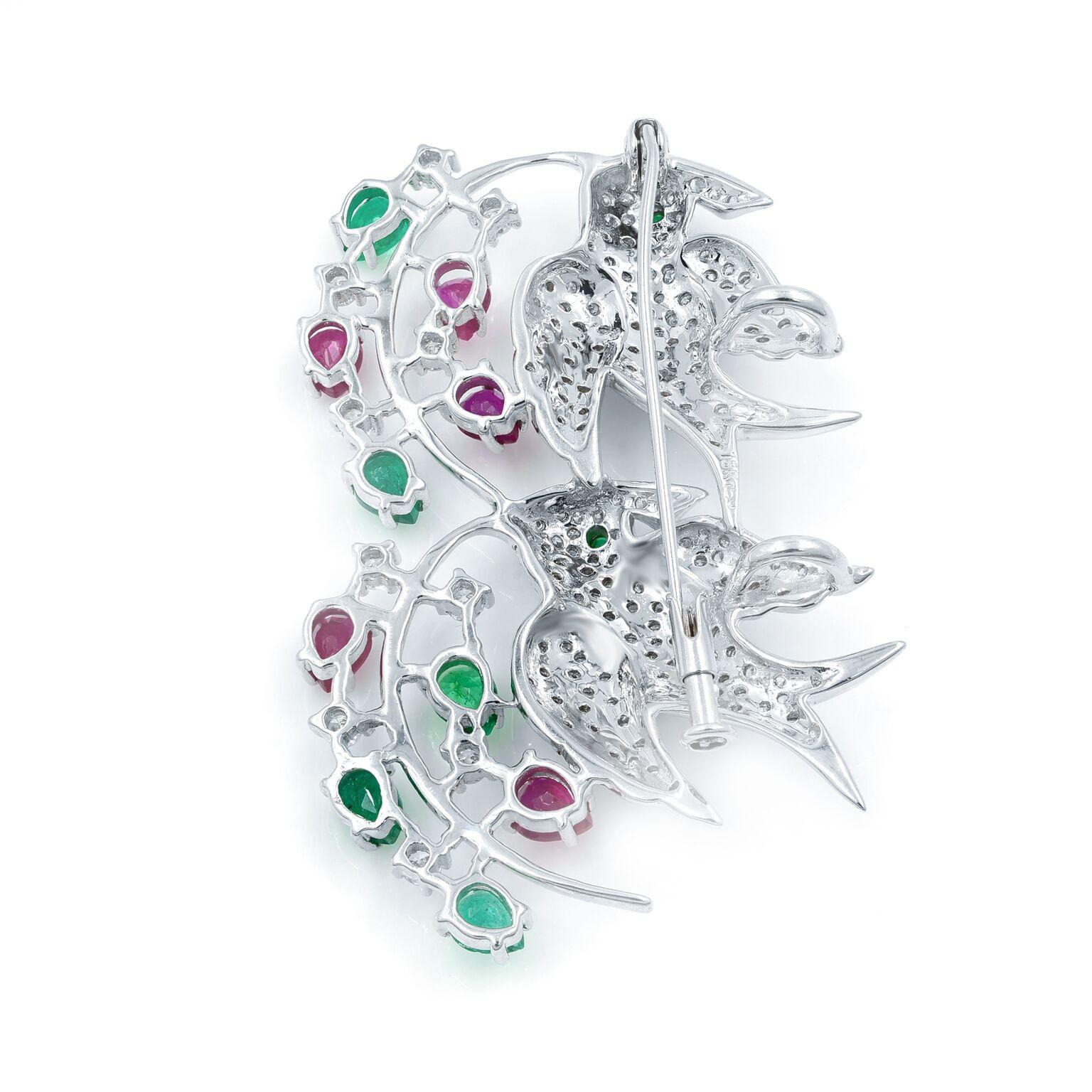 This stunning openwork, 18k white gold brooch is set with glittering diamonds, vibrant emeralds and rubies. This brooch measures 2 1/4 inches tall by 1 7/8 inches wide. The Gemstones are described as follows: 7 Mixed Cut Emeralds weighing 1.56