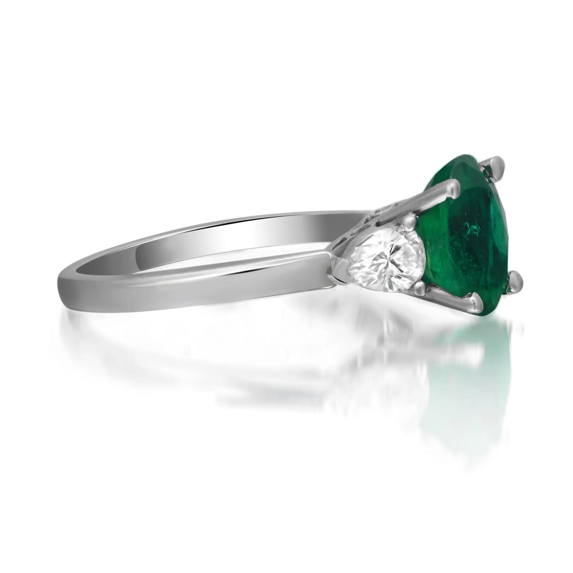 Cette luxueuse bague de fiançailles est ornée d'une émeraude verte ovale sertie au centre et de diamants taille poire de chaque côté en serti clos. Réalisé en platine lustré. Poids total des émeraudes : 1,65 carats. Poids total des diamants : 0,66