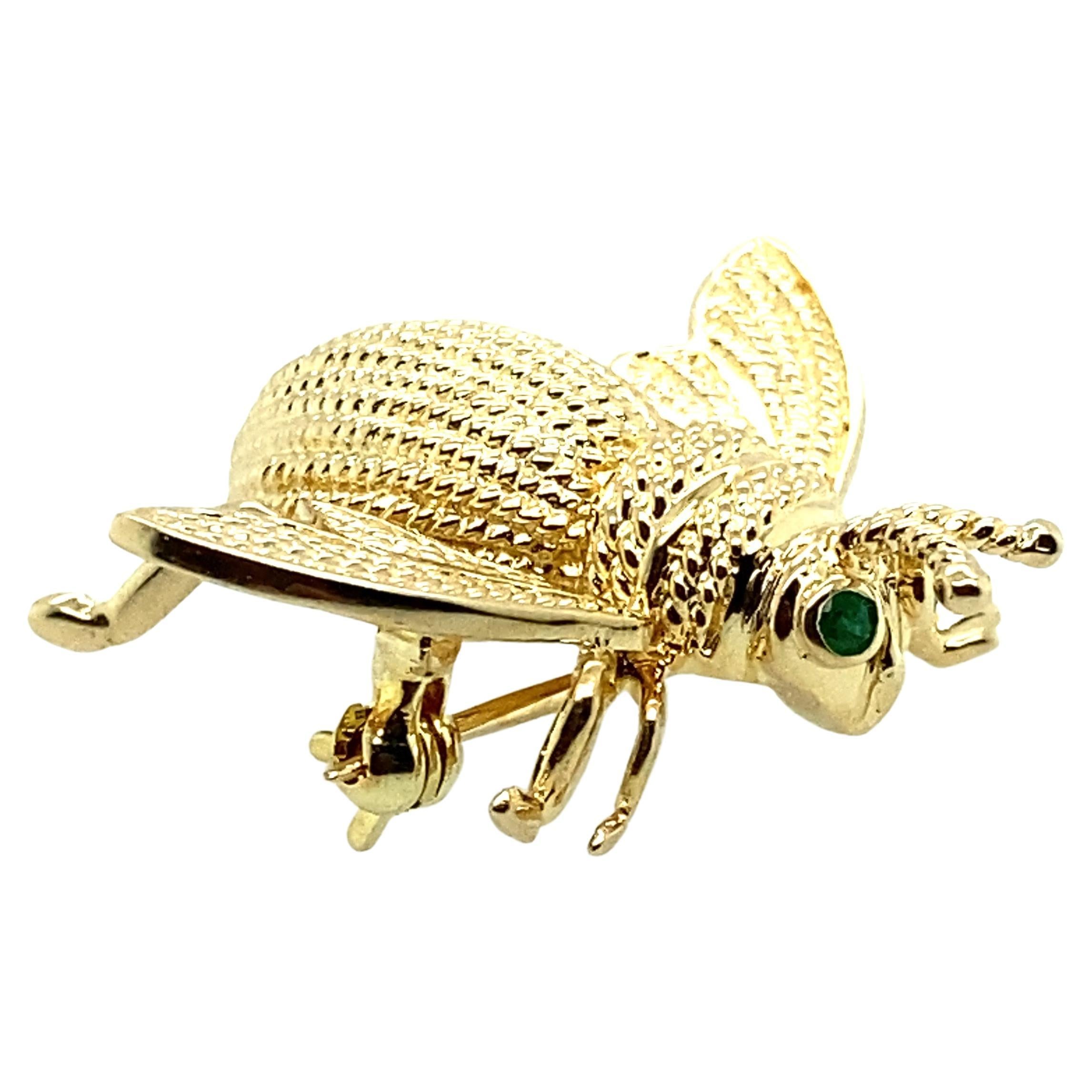 One 14 karat yellow gold fly design pin set with two round natural emeralds measuring just over an inch long and 1.25 inches long complete with a traditional pin closure.
