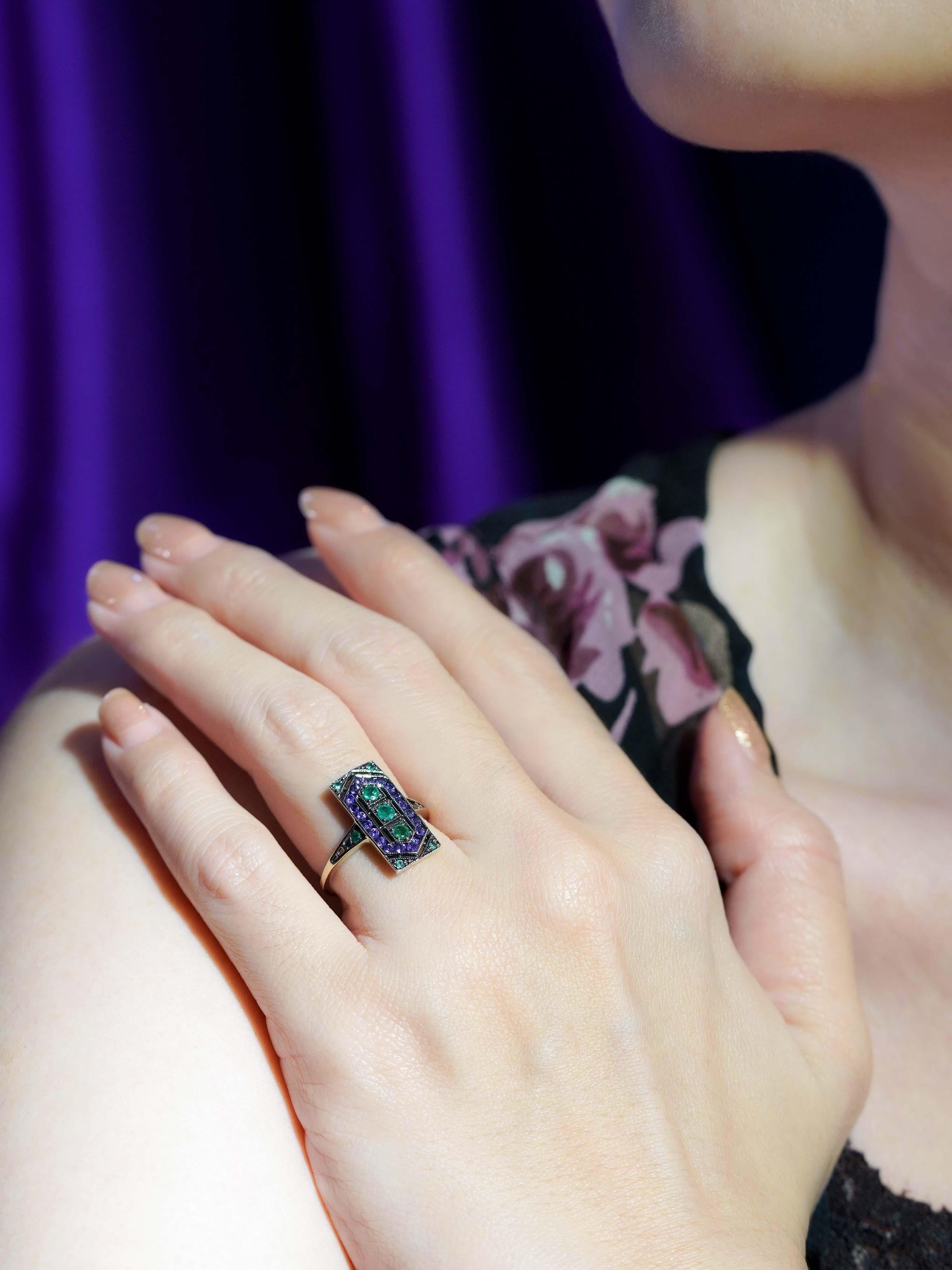 Añade un toque de encanto vintage con este Anillo Estilo Art Decó de Esmeralda y Amatista en Oro Amarillo de 9 K. Con tres vibrantes esmeraldas en el centro, este diseño es rico en color y simetría. Acentuado con profundas amatistas moradas y