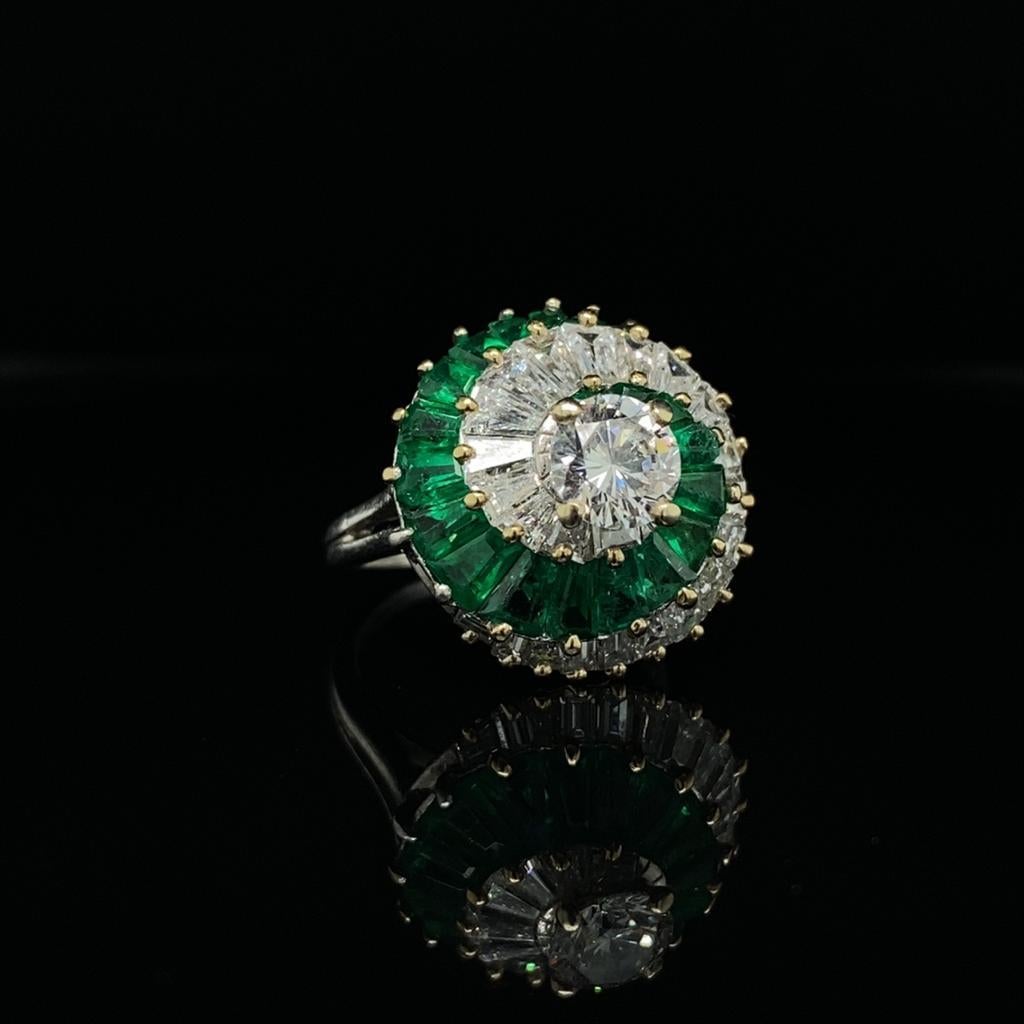 An emerald and diamond 18 karat yellow gold cocktail ring, circa 1960.

Set with a round brilliant cut diamond forming the centre piece to a beautifully handcrafted swirl comprising of calibre baguette cut diamonds and emeralds graduating in