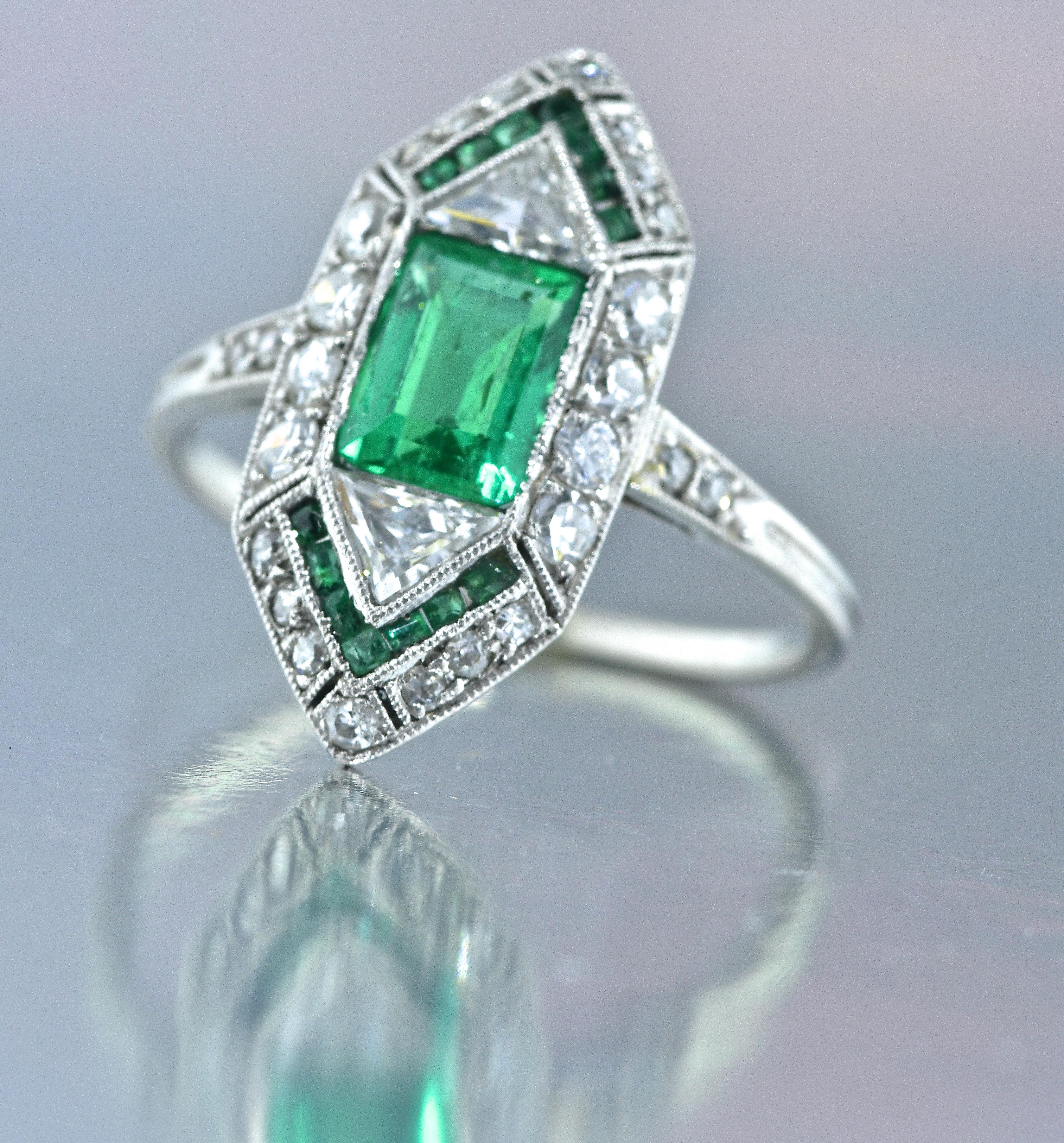 Emeralds in this ring are Colombian and are a vivid pure bright green color.  There are 14 caliber cut smaller matching emeralds.  All of the emeralds are well matched in color.  There are 2 old-cut triangle cut diamonds on either side of the center