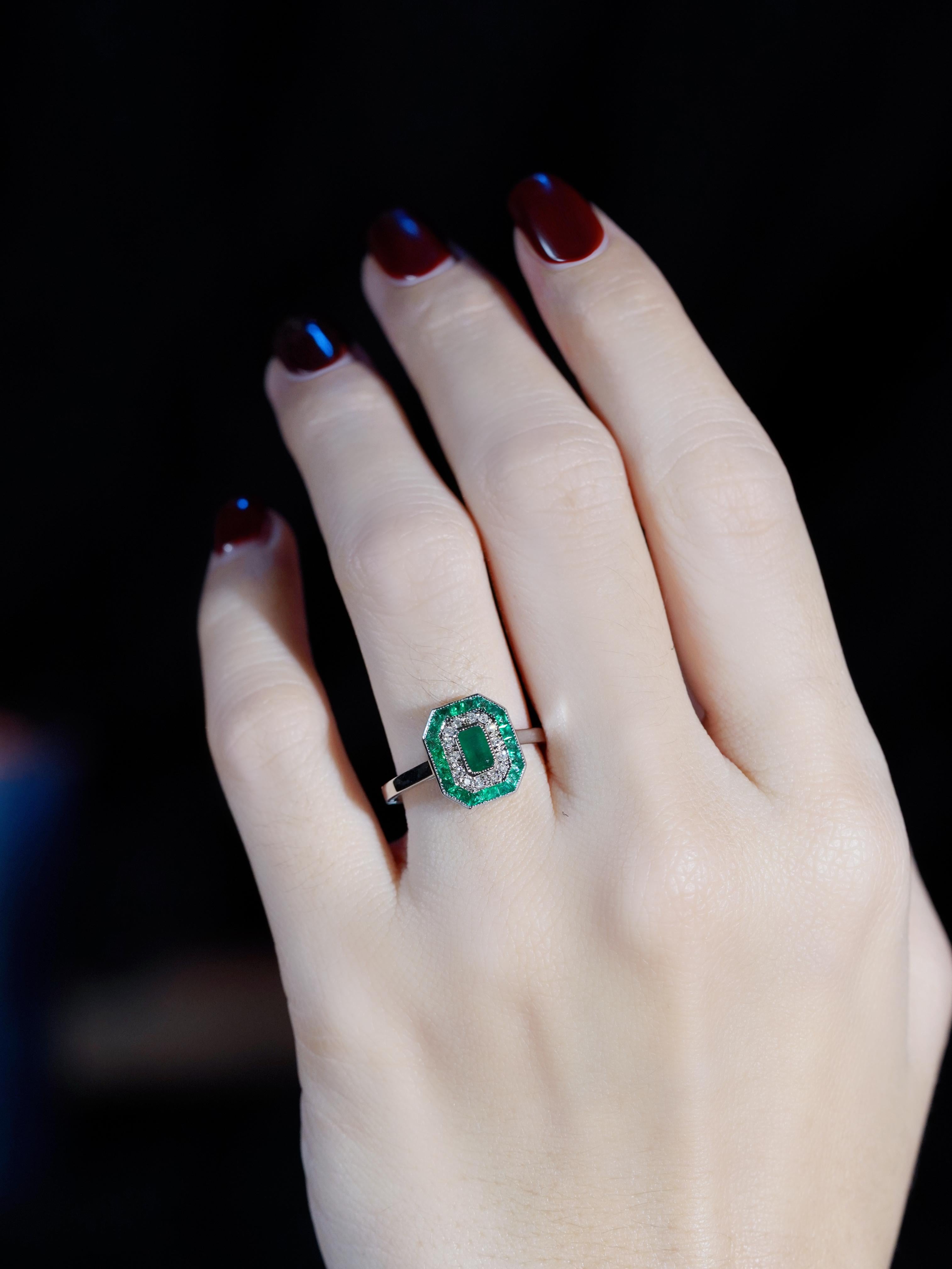 A vibrant emerald takes center stage, glowing with rich, captivating color. It’s beautifully encircled by a halo of sparkling diamonds that add radiant brilliance, while the frame of French-cut emeralds brings a sophisticated touch of vintage