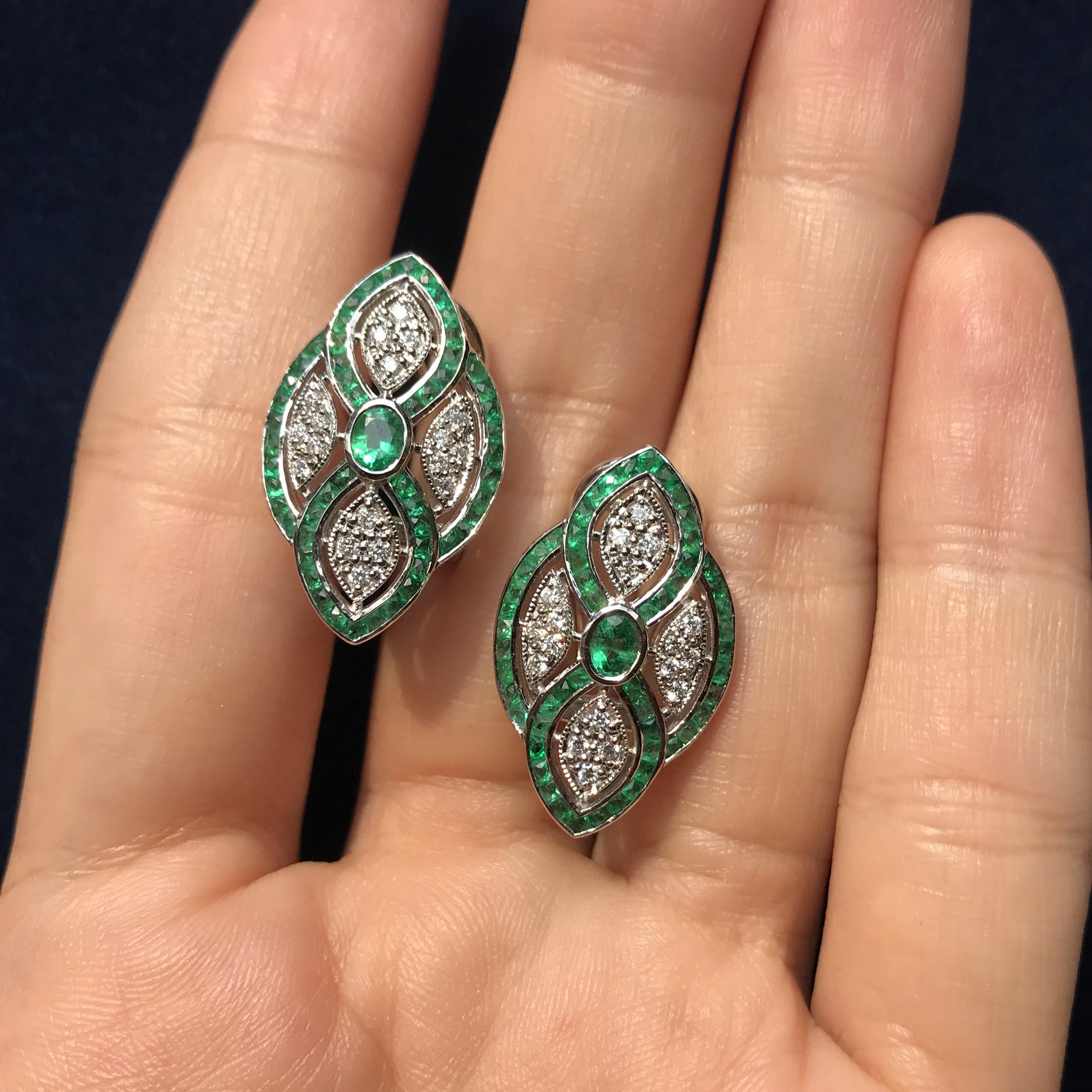 Elégantes boucles d'oreilles florales de style Art déco avec au centre une émeraude vibrante représentant l'étamine. Autour d'elle, des pétales de diamants ajoutent de l'éclat et du contraste. Les boucles d'oreilles sont encadrées d'émeraudes