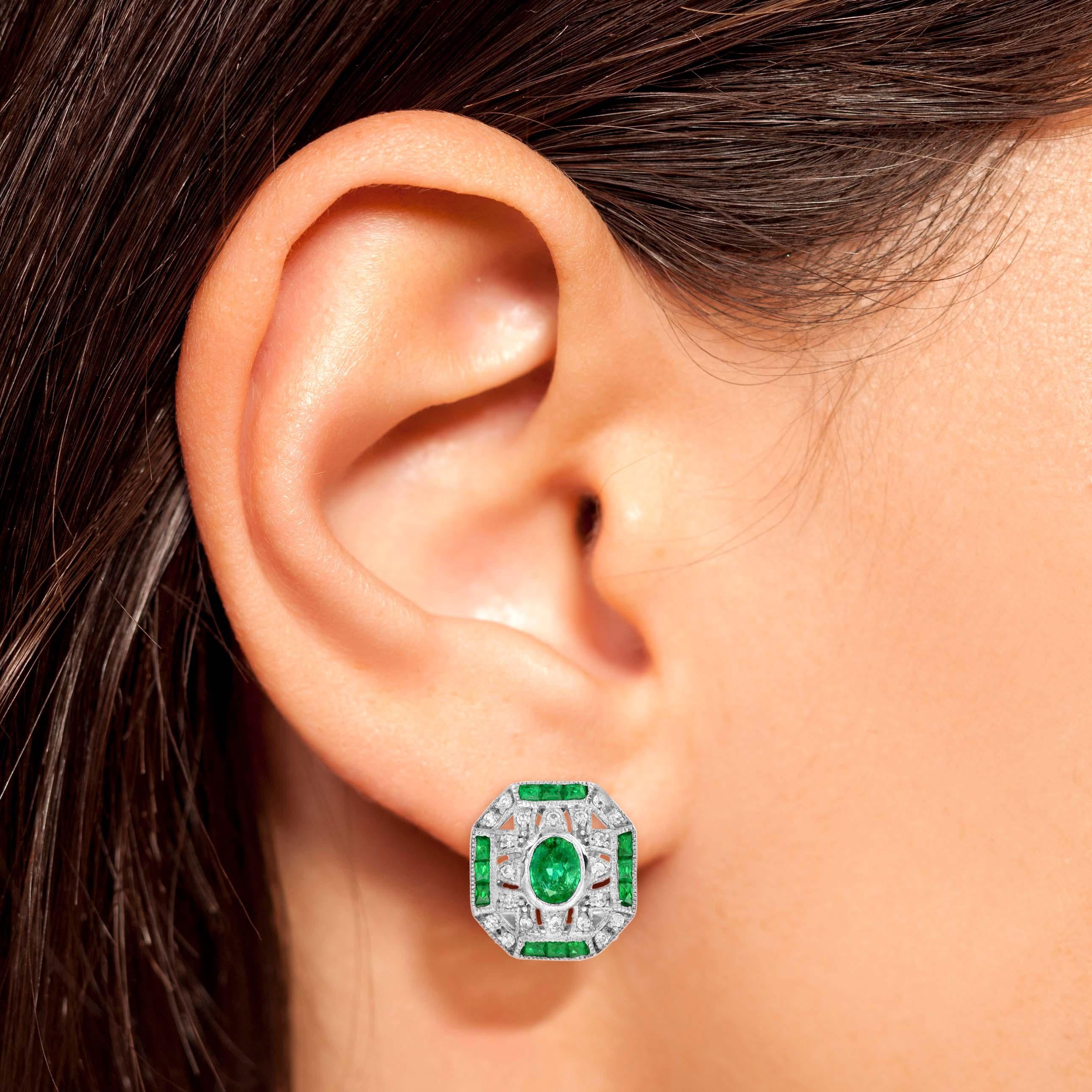 An Art Deco inspired emerald and diamond white gold omega back earrings. Featuring one oval shaped emerald of approximately 0.70 carat each. Accented by 24 French cut emeralds and 40 round cut diamonds on each side. Wear this earrings daily to add a
