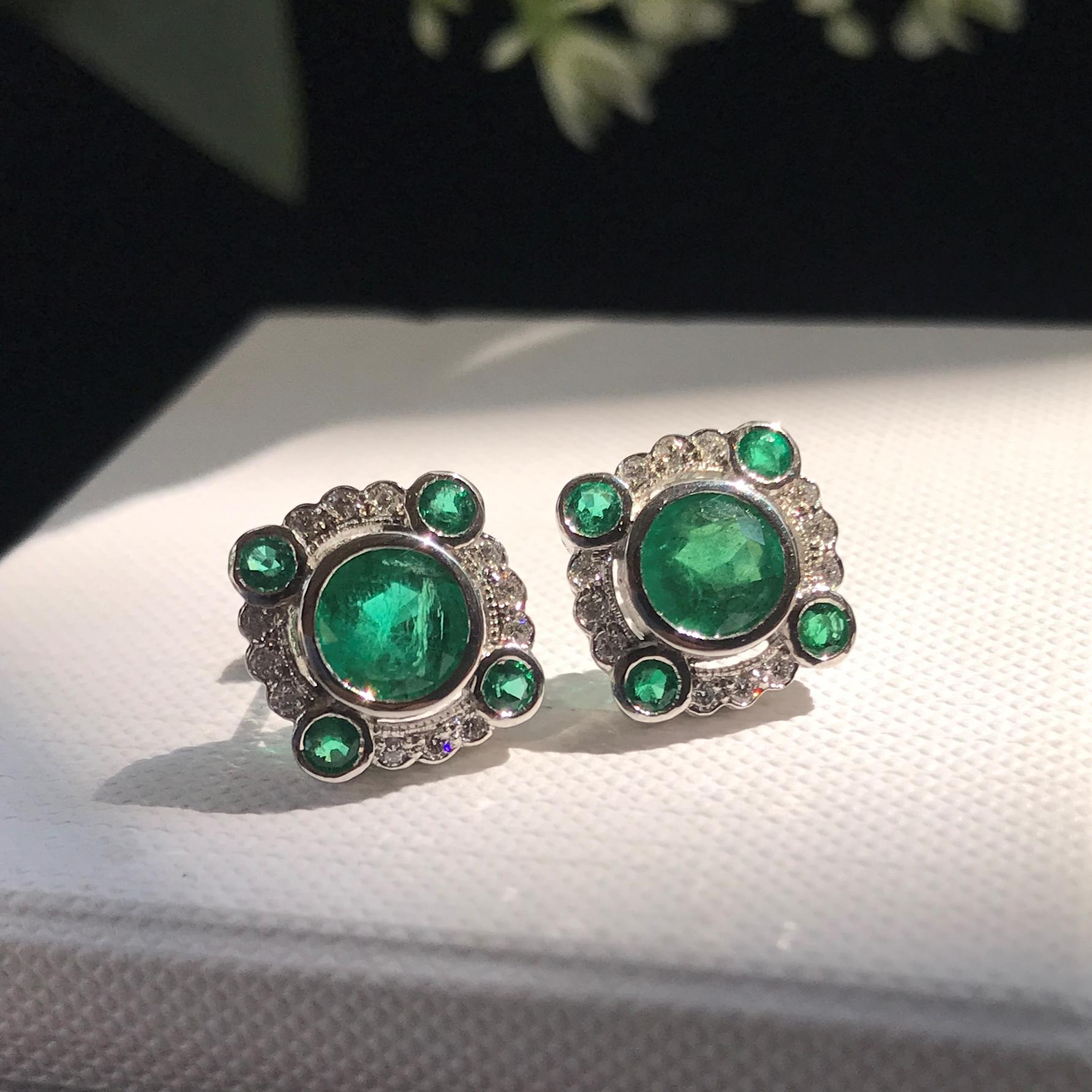 Eleva la tua eleganza con gli orecchini con smeraldo e diamante in stile Art Deco. Caratterizzato da uno smeraldo rotondo brillante al centro, circondato da diamanti e accentuato da smeraldi più piccoli ad ogni angolo. L'intricato design Art Déco