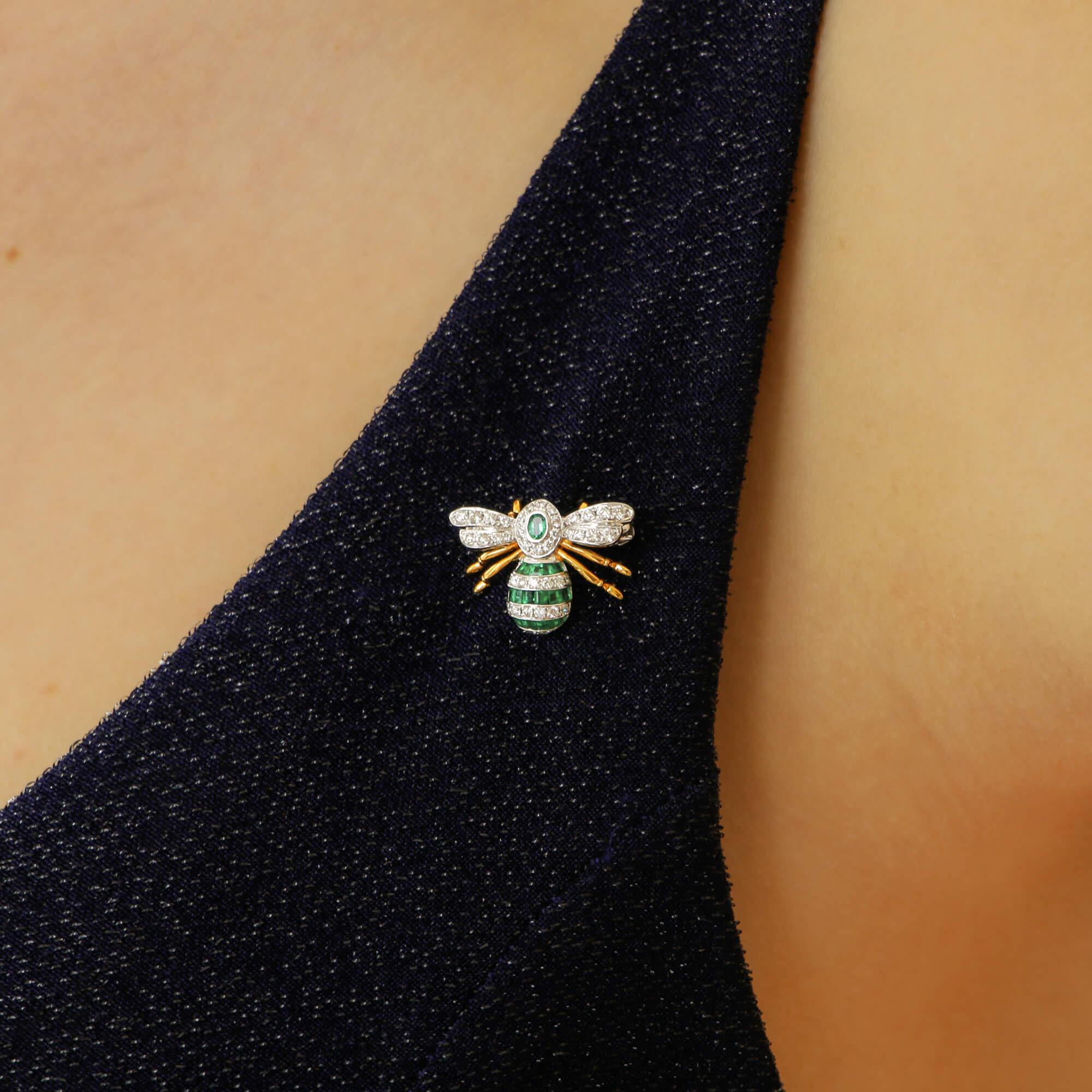 Eine wunderschöne handgefertigte Bienenbrosche mit Smaragd und Diamanten aus 18 Karat Weiß- und Gelbgold. 

Der Thorax der Biene besteht aus einem ovalen Smaragd in Rubover-Fassung in einem Halo aus körnig gefassten runden Brillanten, die Flügel