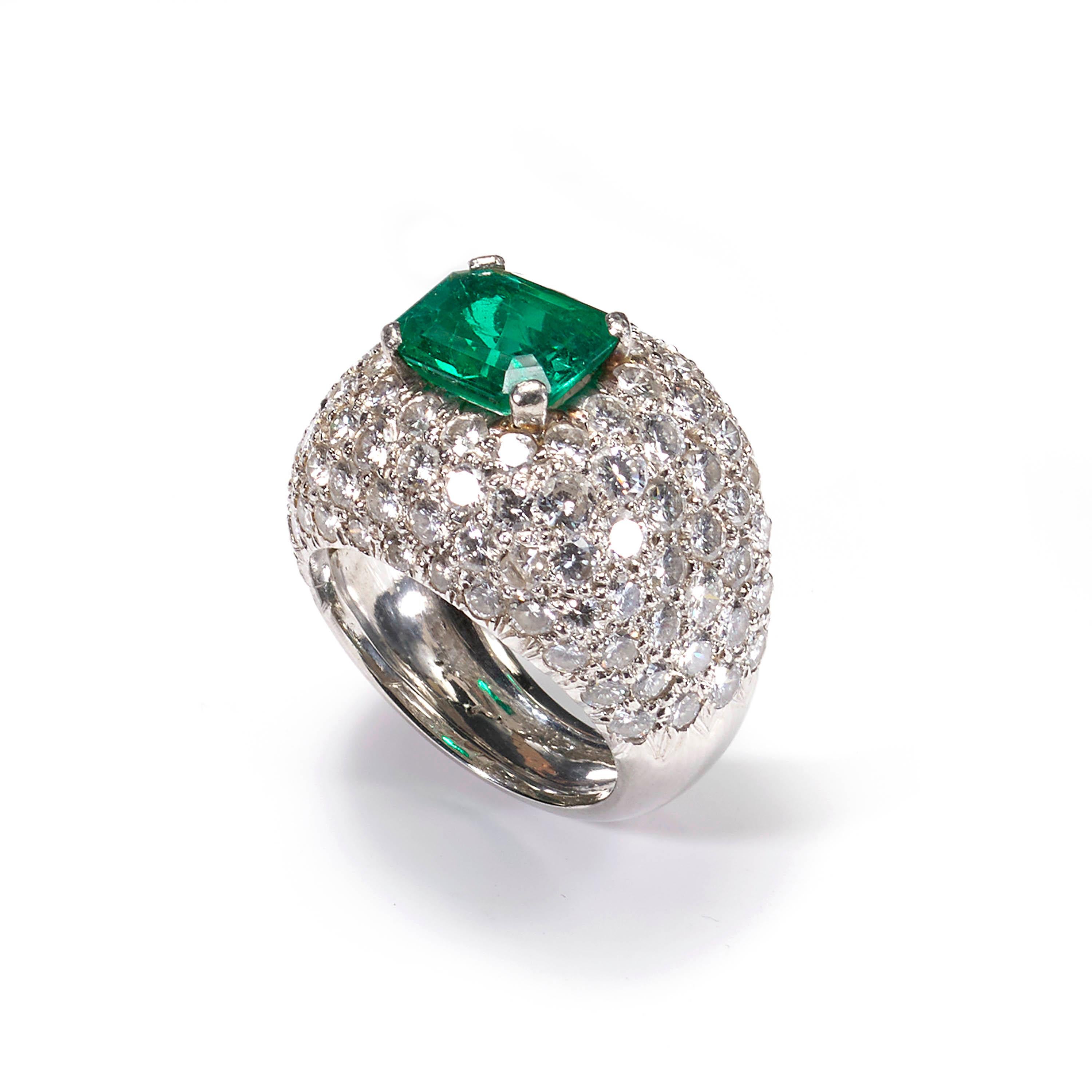 A modern emerald and diamond fancy bombé style ring, centrally claw set with an emerald-cut emerald, weighing an estimated 2.40 carats, surrounded by brilliant-cut diamonds in a pavé setting, weighing an estimated total of 6.00 carats, all mounted