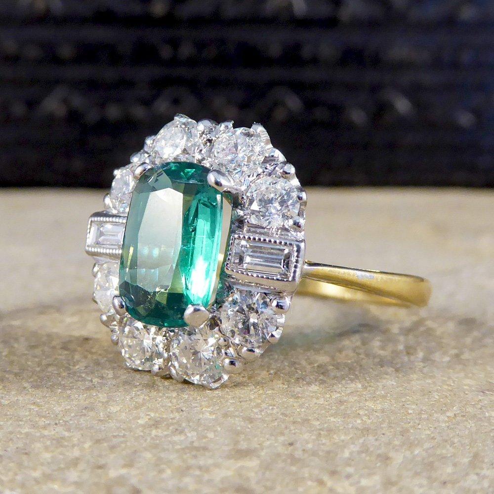 This contemporary design contains a one carat Colombian emerald centre stone, adorned with a diamond cluster halo of four brilliant cut diamonds above and below, separated by two baguette cut diamonds.  The centre setting is 18 carat white gold,