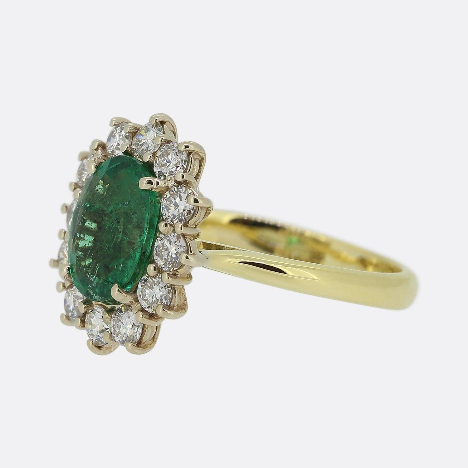 Here we have a wonderful emerald and diamond cluster ring. Crafted from 18ct yellow gold, this ring features a centralised oval shaped emerald which possesses a intense vivid green colour tone. This focal stone is highly complimented by a cluster of