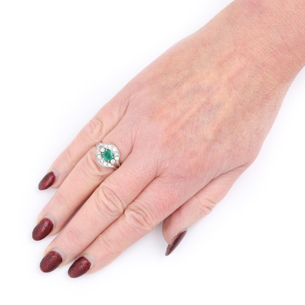 A distinctive 18 Karat white gold emerald and diamond cluster ring which was made circa. 1970. The round emerald measures estimated 0.80ct and is surmounted by 1 carat of round brilliant cut diamonds. The setting of the ring with ‘V’ shape indented