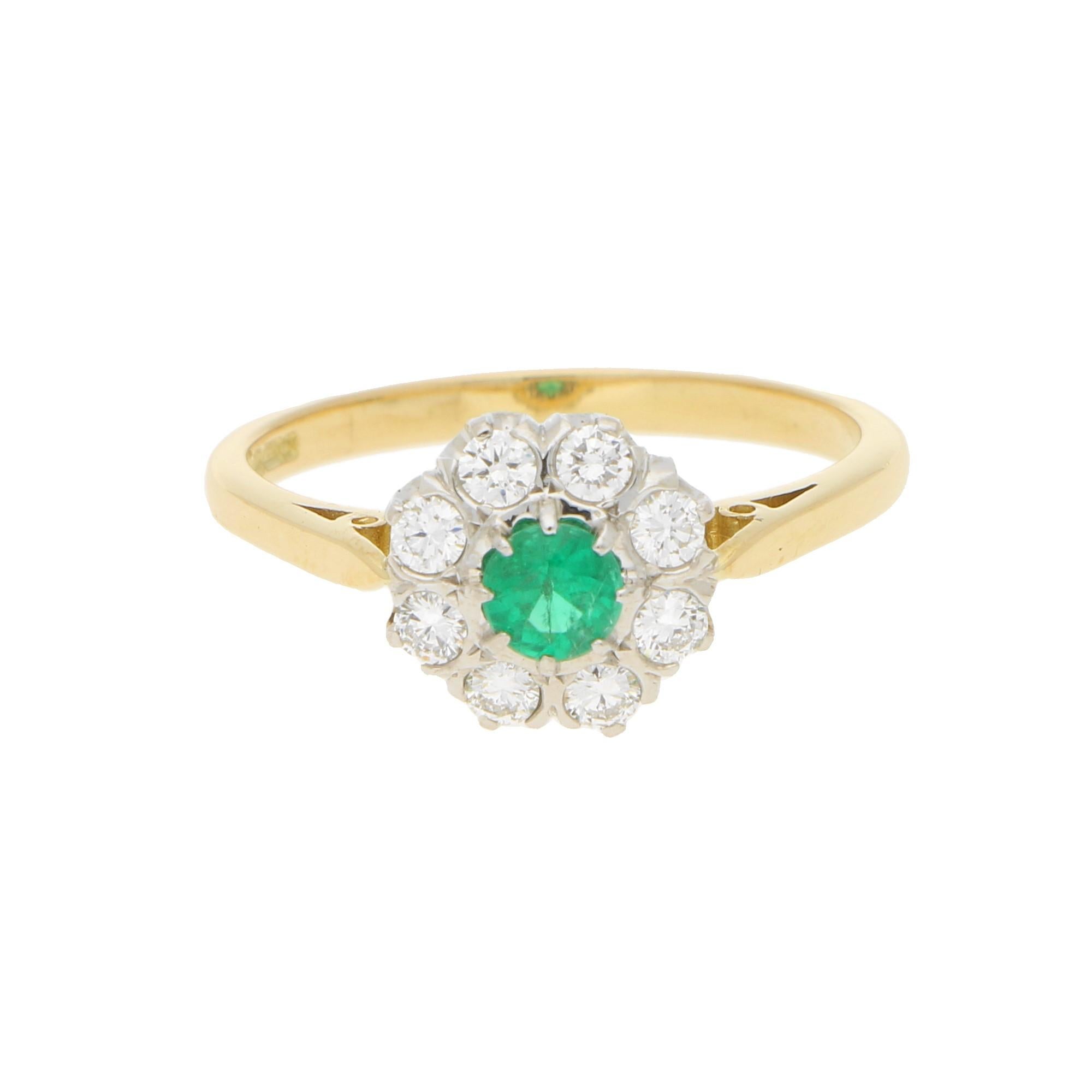 A beautiful little emerald and diamond daisy cluster ring set in 18k yellow and white gold. 

The piece is centrally set with a vibrant round cut green emerald eight claw set in an open back slightly raised setting. The emerald is the surrounded by