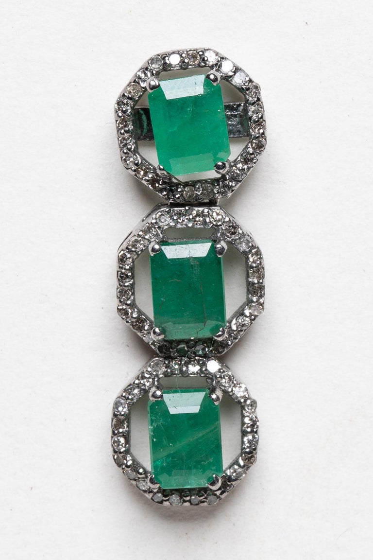 A pair of triple drop, emerald-cut Columbian emerald earrings. Emeralds are surrounded by round, brilliant cut diamonds in a pave` setting in an oxidized sterling silver in a subtle octagonal shape.  Post backs for pierced ears.  Carat weight of