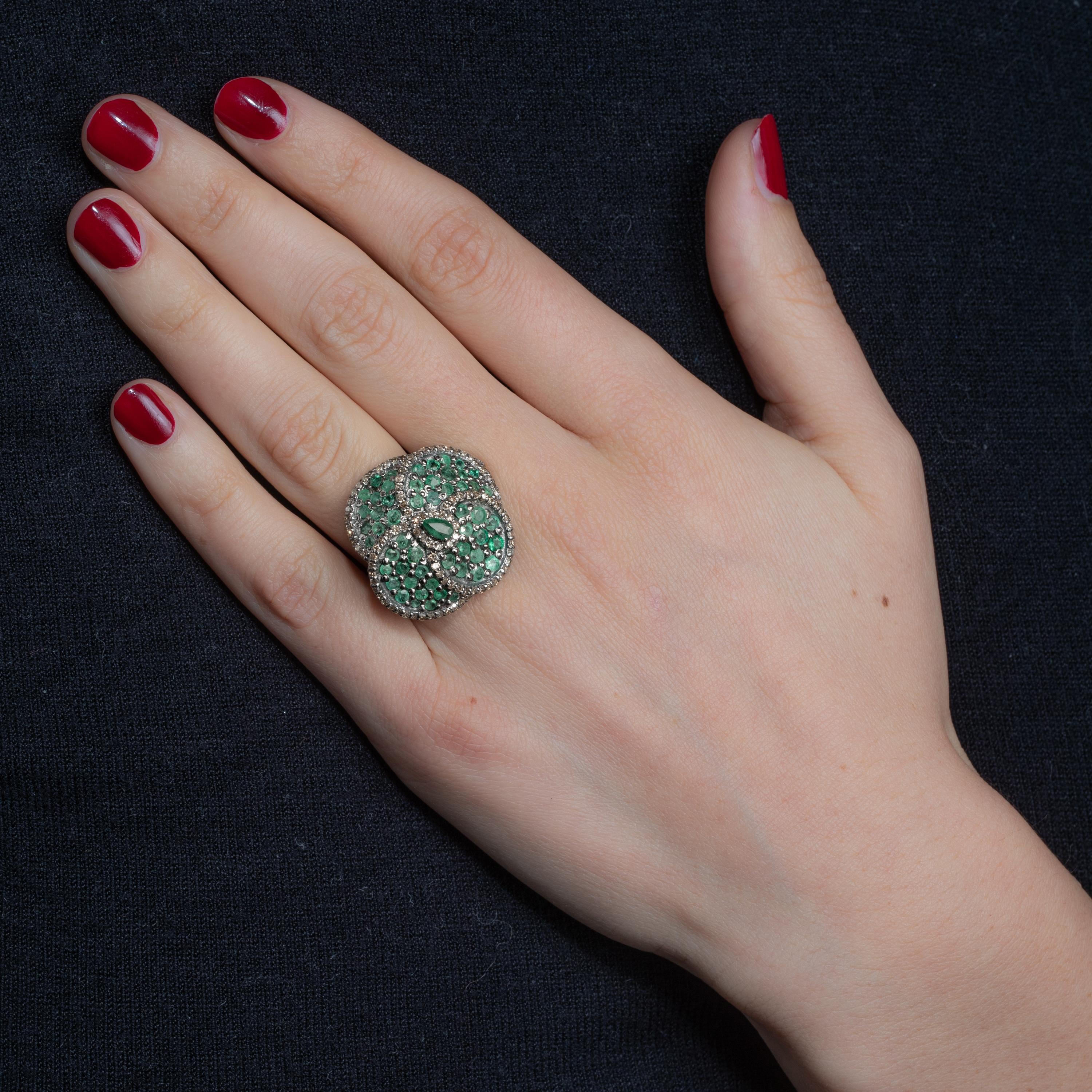 A stunning flower petal ring with round-cut emeralds and a faceted pear-shaped emerald at the center.  Each petal bordered with pave`-set diamonds.  Set in oxidized sterling silver.  Ring size is 7.  Carat weight of emeralds is 2.89; diamonds are