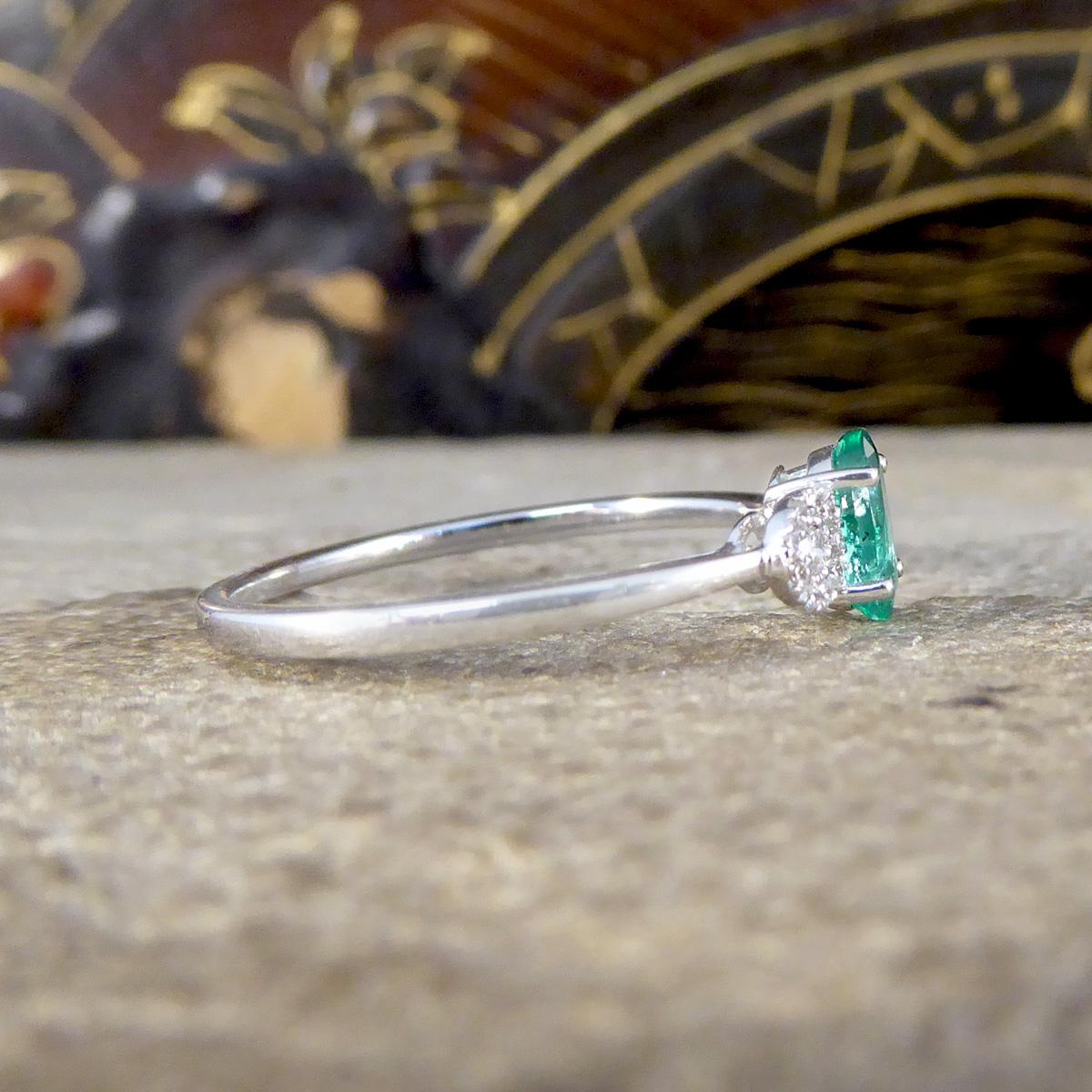 A beautiful and bright three stone illusion ring. Featuring in the centre of this new ring is a 0.38ct bright green Emerald with typical Emeralds flaws in a four claw basket setting accompanied by a Diamond cluster on either side. The Diamond