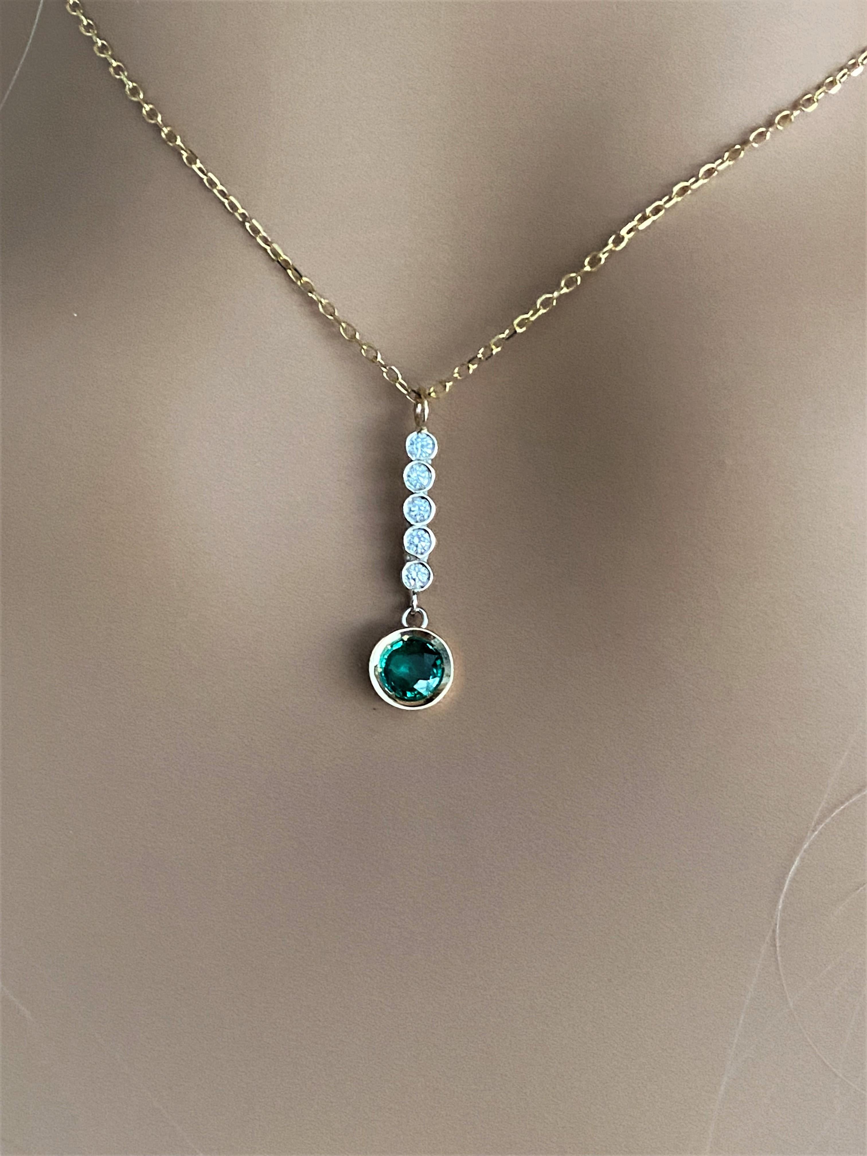 Fourteen karats white and yellow gold trending lariat necklace pendant 
One round emerald bezel set weighing 0.40 carats
Drop diamond bar weighing 0.10 
Emerald hue tone color grass green
Chain measuring 16 inches long
Diamond drop lariat measuring