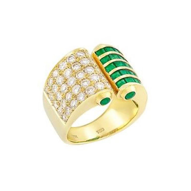 An extremely lively and unique design of a slightly open ring accented with emeralds and diamonds in 18K Yellow Gold. The ring consists of 35 round diamonds (appx. 1.20 cts.), square-cut emeralds, and 4 round cabochon emeralds on the sides. 