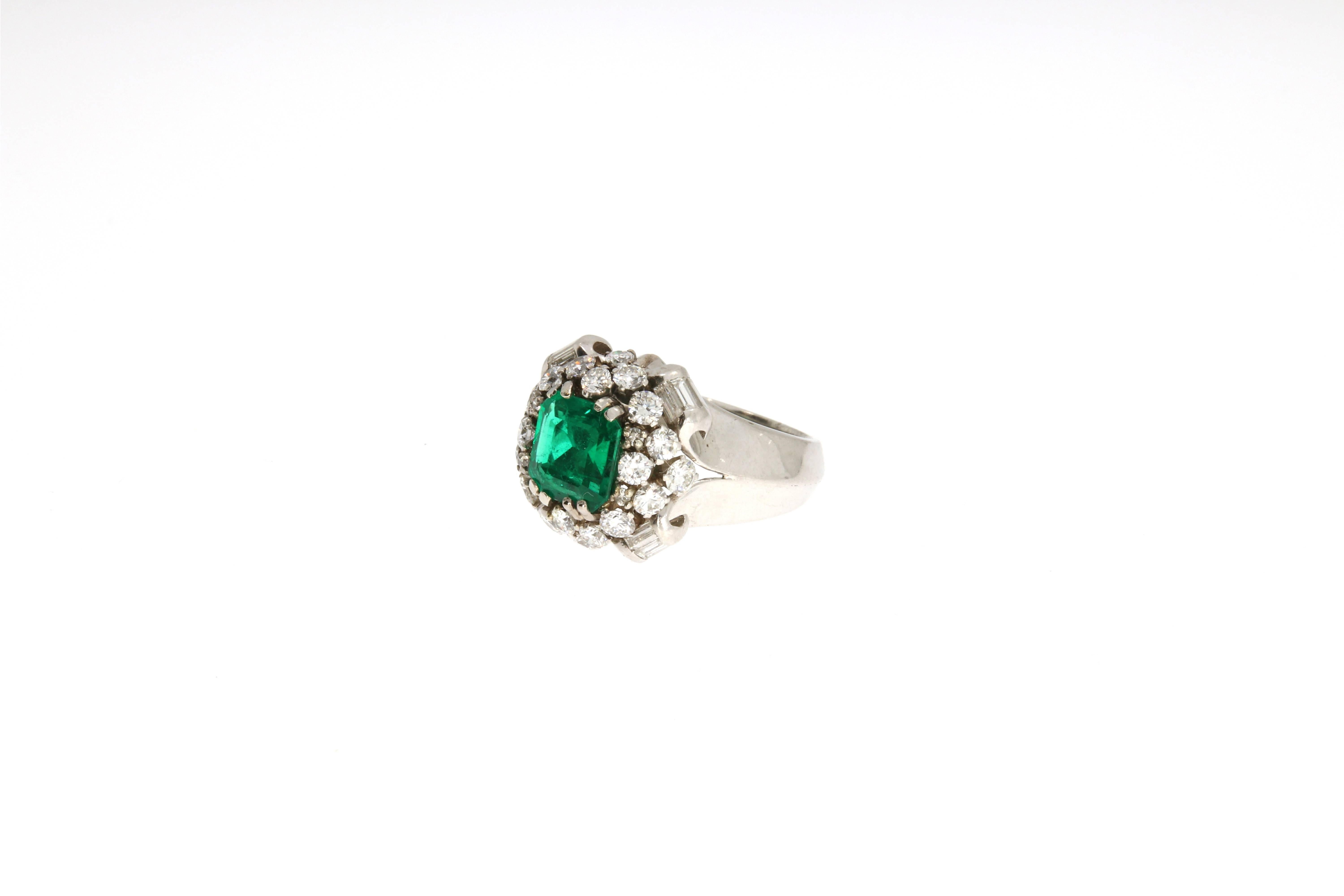 An impressive platinum cocktail ring. It is centered by a step- cut emerald (no oil) within a surround of 24 brilliant cut diamonds (in total approx: 1.65 ct). The refined setting is accentuated by 12 baguette diamonds (in total approx: 0.5 ct)