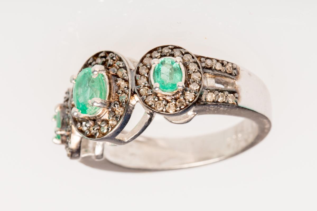 Faceted, oval Columbian emeralds bordered in pave`-set diamonds.  Sterling silver band.  Carat weight of diamonds is .50, emeralds .70.  Ring size is 6.5.