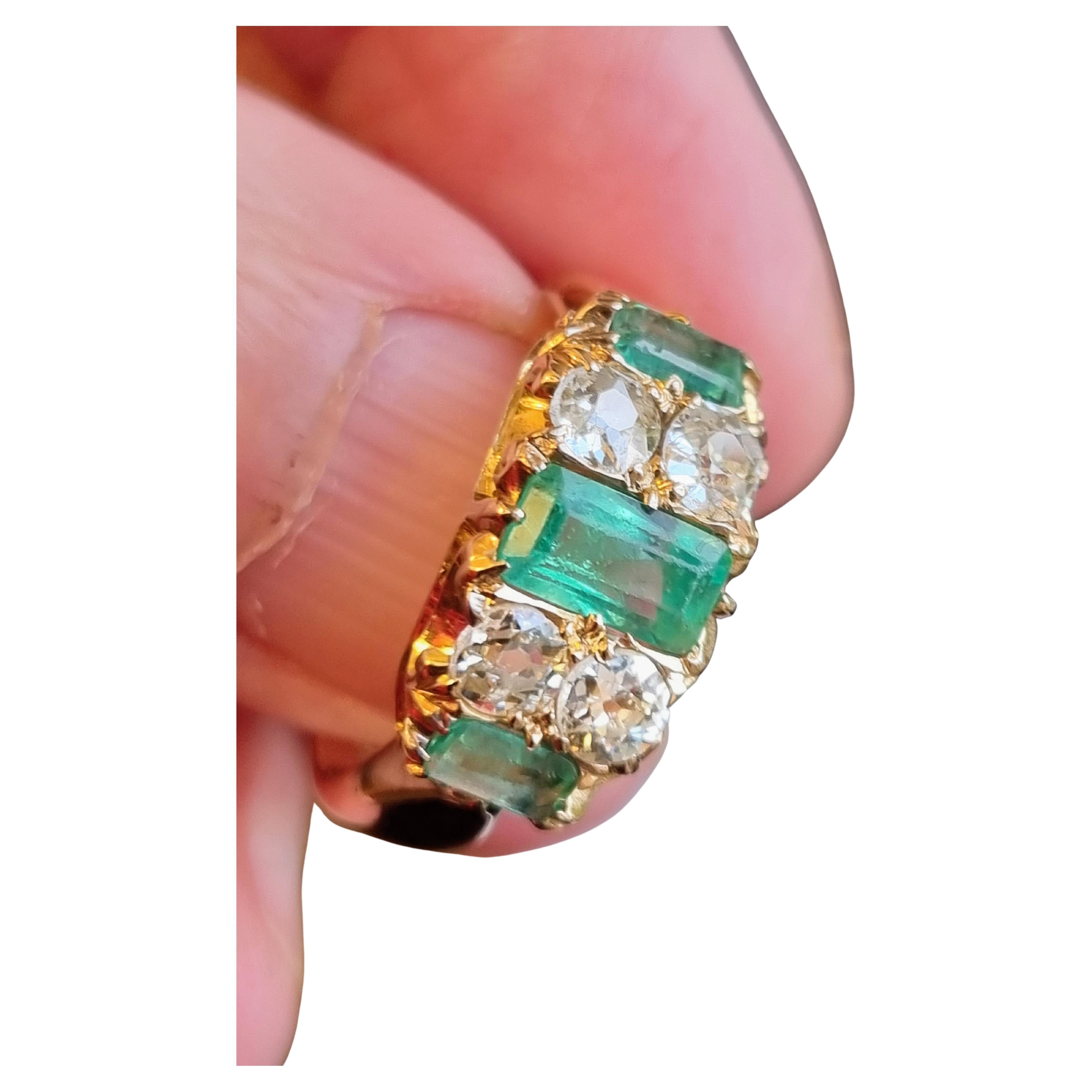 A fine Australian goldfields period ring, signed G. R. Addis, crafted in yellow gold. The ring is designed with a central emerald-cut emerald of vibrant green colour, flanked by old mine-cut diamonds, and further accented by two rectangular step-cut