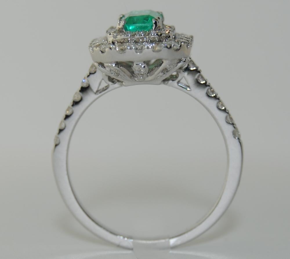 Ladies Ring with a center Emerald weighing 0.79 carat, surrounded by Brilliant Round White Diamonds total weight 0.91 carat.  This ring is mounted in 18 Karat White Gold.  Size 7.