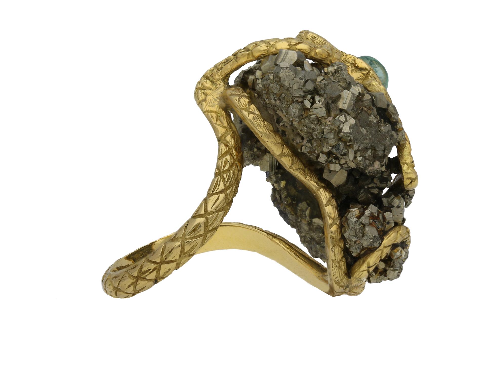 Emerald and pyrite snake ring. Set with one round cabochon natural unenhanced emerald in an open back rubover setting with an approximate weight of 0.25 carats, further set with a pyrite cluster, to an unusual snake design depicting a serpent coiled