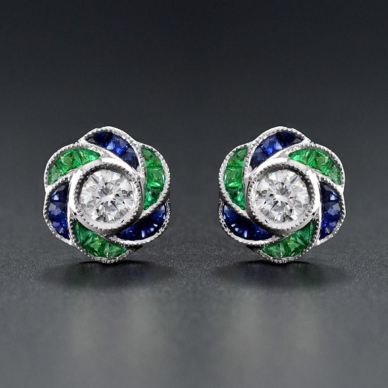 Perfect with everyday wear, these charming vintage Art Deco revivalist design stud earrings feature a pair of brilliant cut diamonds surrounded by bright blue sapphire and emerald for rose petals finished look all in 18K white