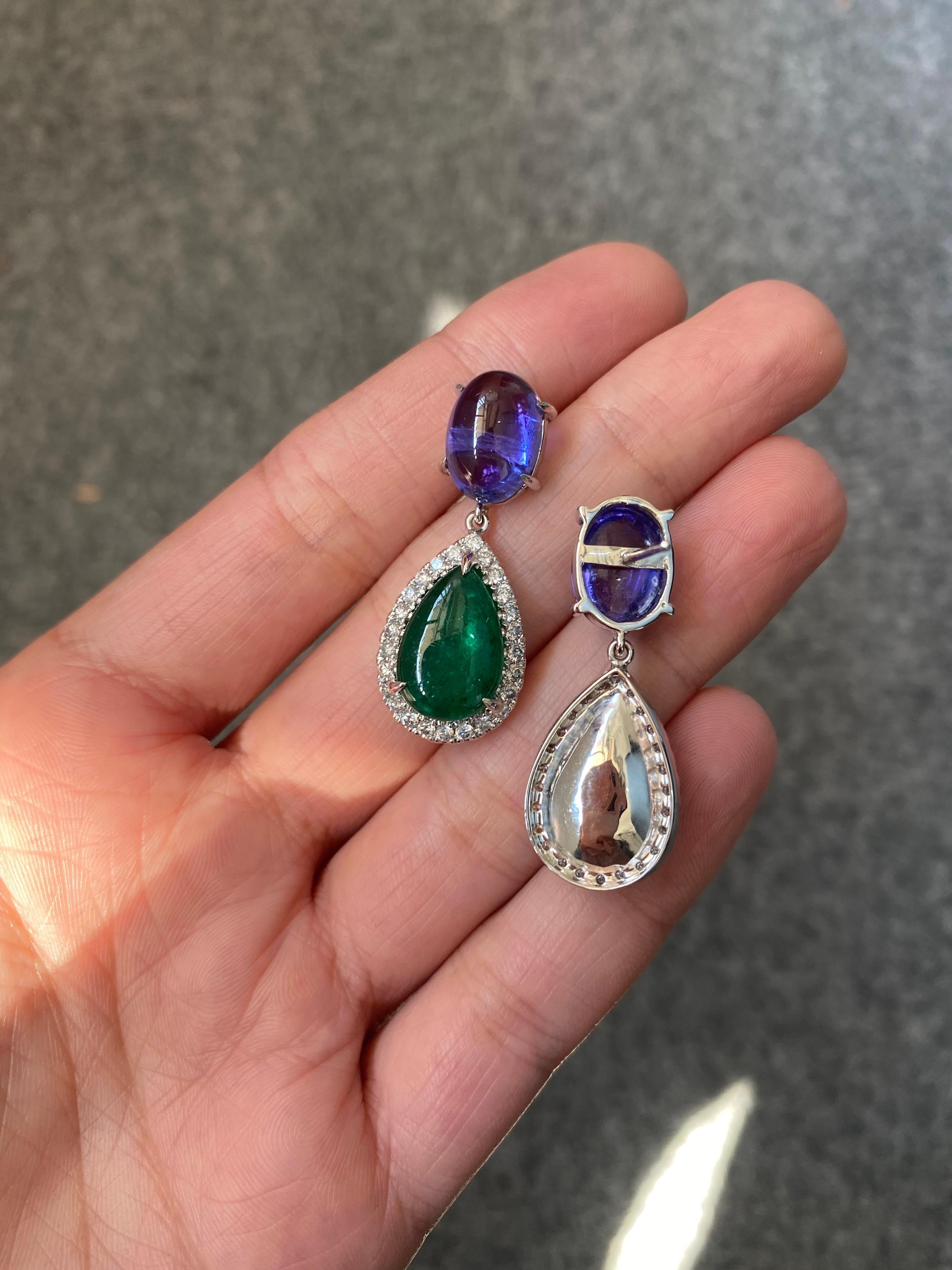 A beautiful combination of natural 10.84 carat Tanzanite cabochons and 10.89 carat pear shape natural Emerald cabochon, set in 18K White Gold with Diamonds. The gemstones are transparent and have great luster and color to them. The earrings are