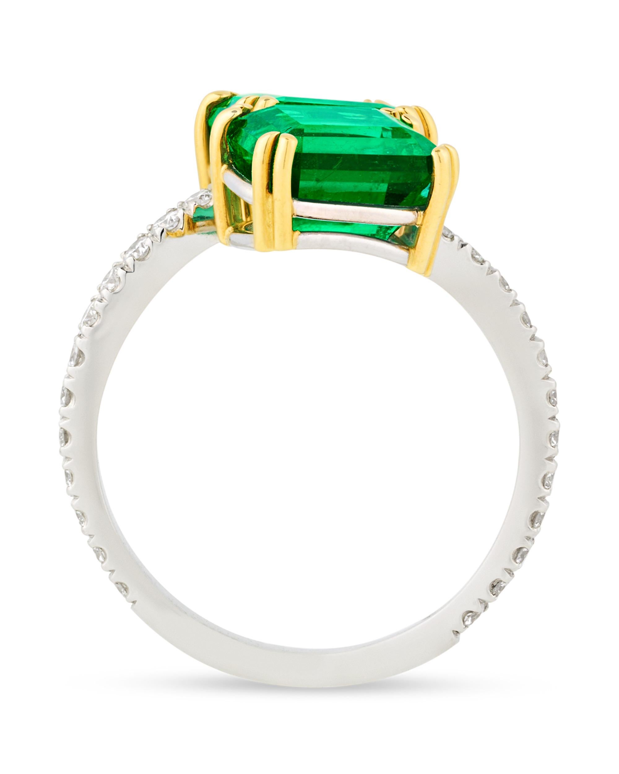 Taking a unique bypass design, this elegant ring features two verdant green emeralds. Certified by the American Gemological Laboratories as originating in Zambia, the emerald-cut gemstones weigh 2.60 carats and 2.56 carats respectively and show only