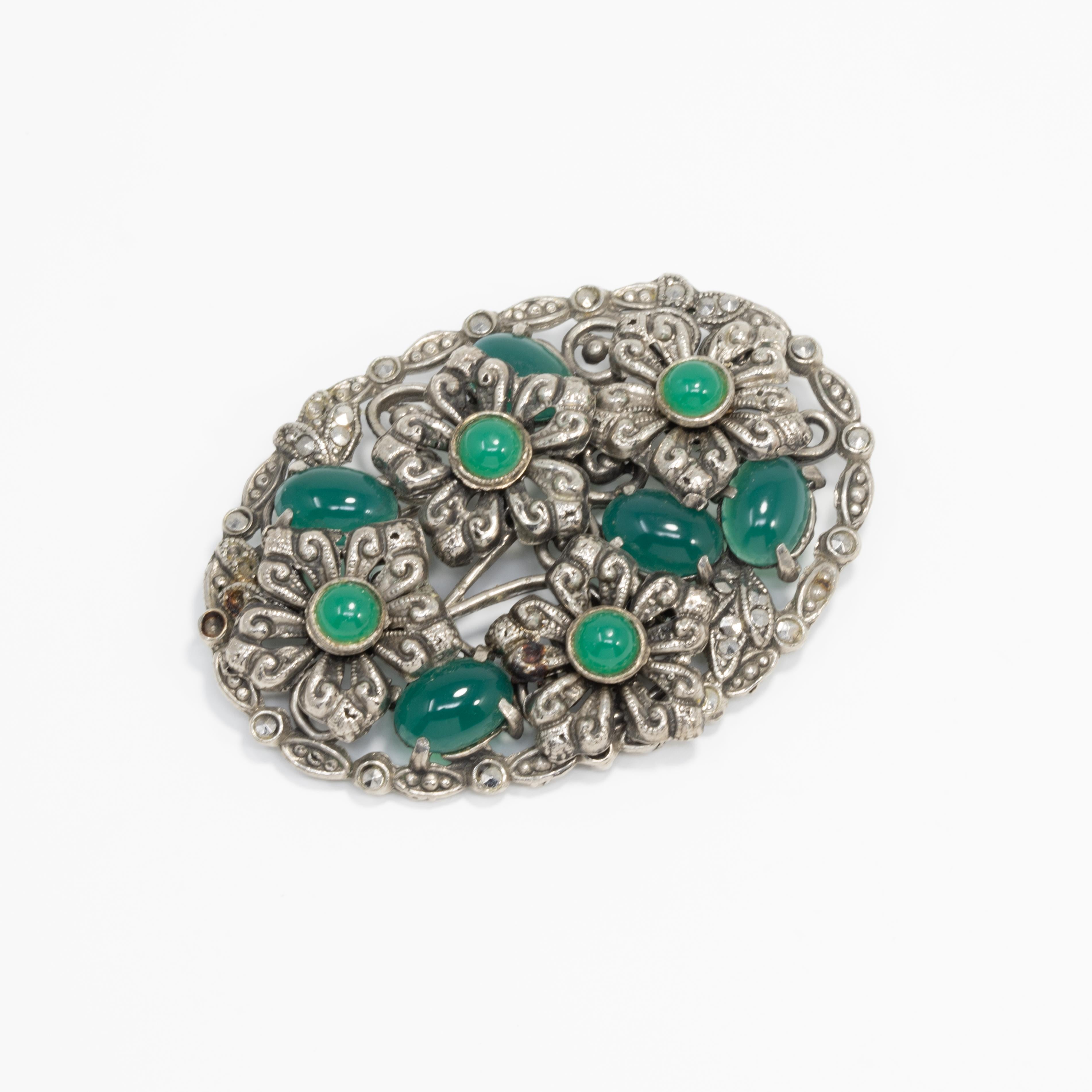 Vintage collectors' pin, featuring opaque emerald-colored cabochons set in an flower-decorated oval pin brooch. Silver-tone.

Dated early 1900s based on pin rollover mechanism.