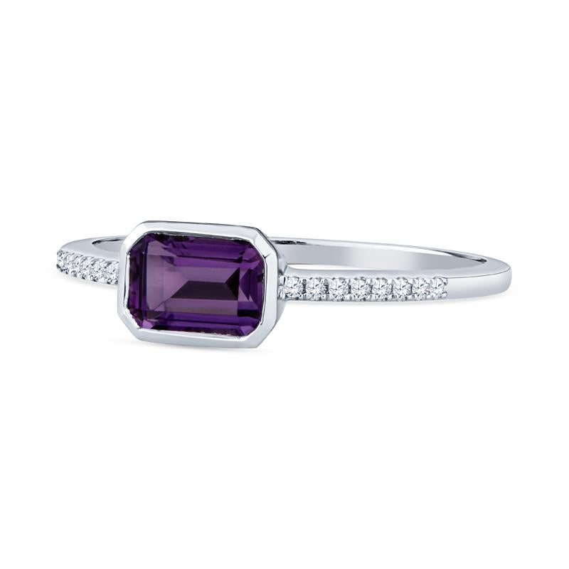 This dainty ring features an emerald cut amethyst set east-west accented by 0.04 carat total weight in round diamonds on the band set in 14 karat white gold. It is a size 6.5 but can be resized upon request. This ring can be worn alone or stacked